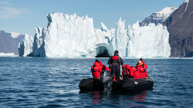 Ein Boot mit Passagieren fährt auf dem Wasser vor einer Gletscher- und Bergkulisse in der Antarktis.