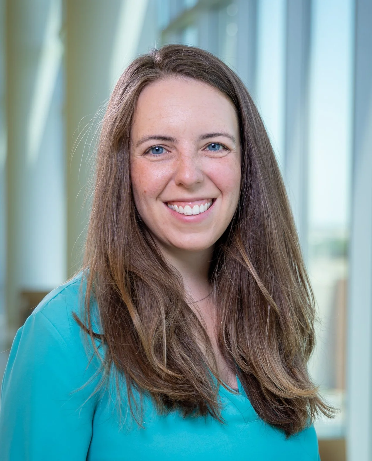 Woman with long straight hair and blue eyes wearing a teal shirt