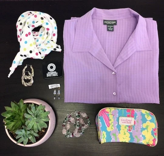 A colorful blouse, scarf, accessories, makeup bag, and potted succulent on a brown tabletop.  
