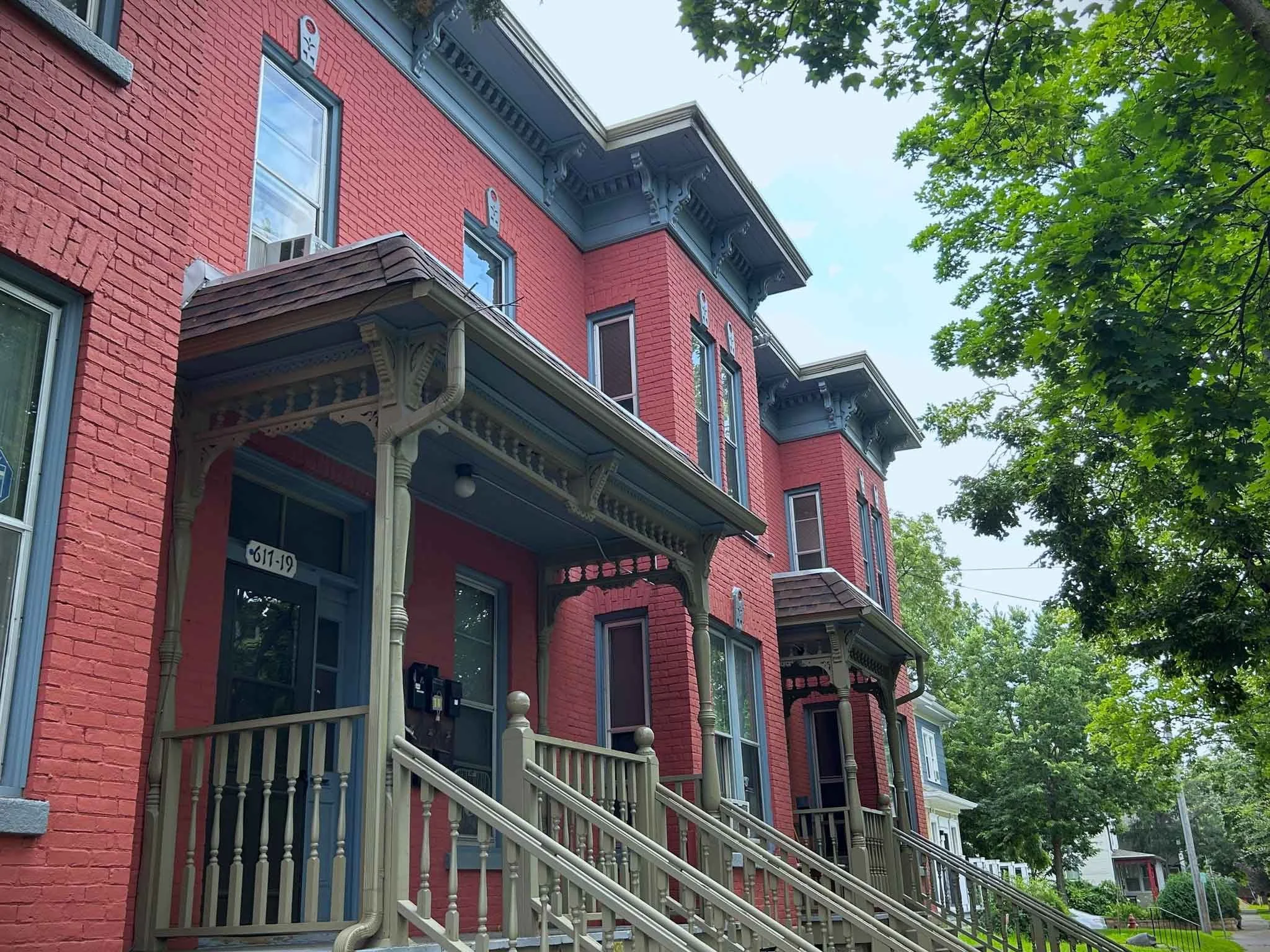 The exterior of a red brick apartment building on a tree-lined street.