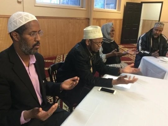 People sitting at a table with their hands upturned and eyes closed, praying. 