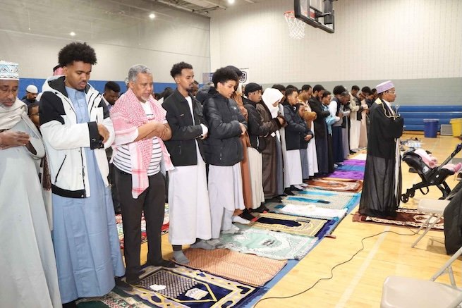 People standing on individual prayer mats in a room, facing towards Mecca and praying.
