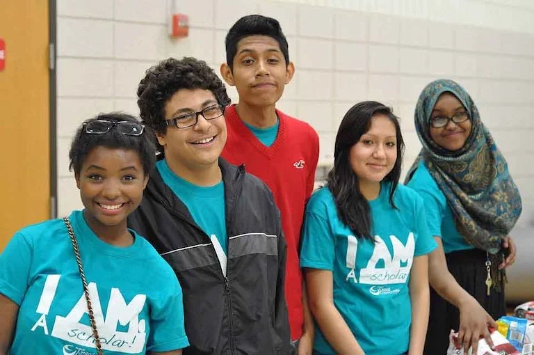 A group of four kids smiling at the camera and inside a community center.