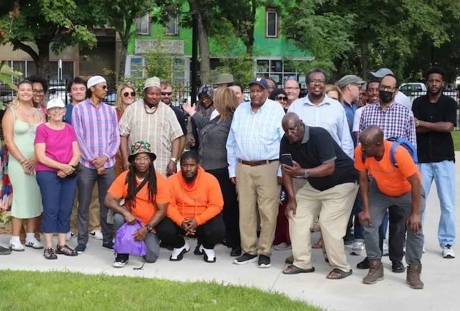 A large group of people standing outside and posing for the camera, with a green building behind them.