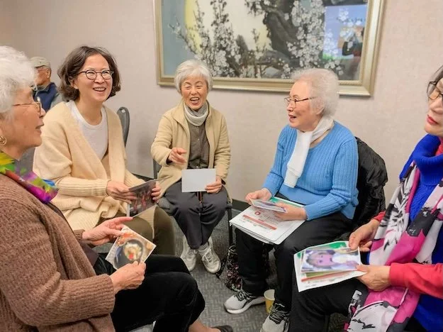 Elderly people sitting in a circle on chairs and smiling. 
