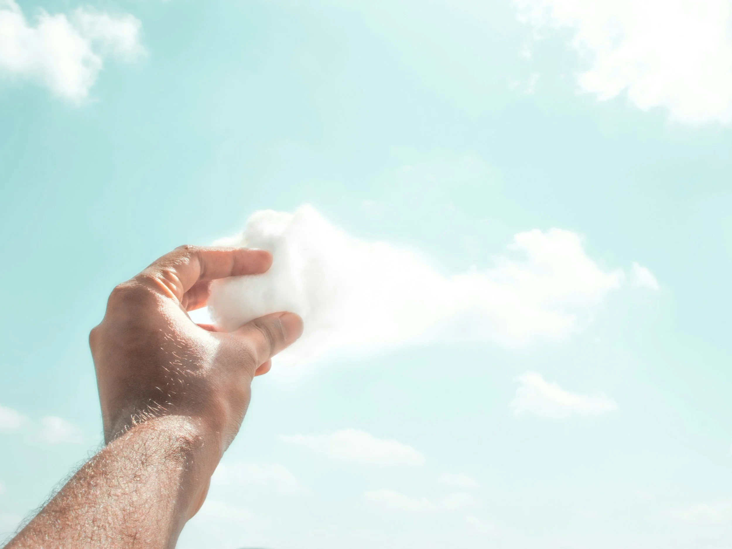 A male hand reaches towards the sky and grabs a piece of the clouds, pulling it downward.