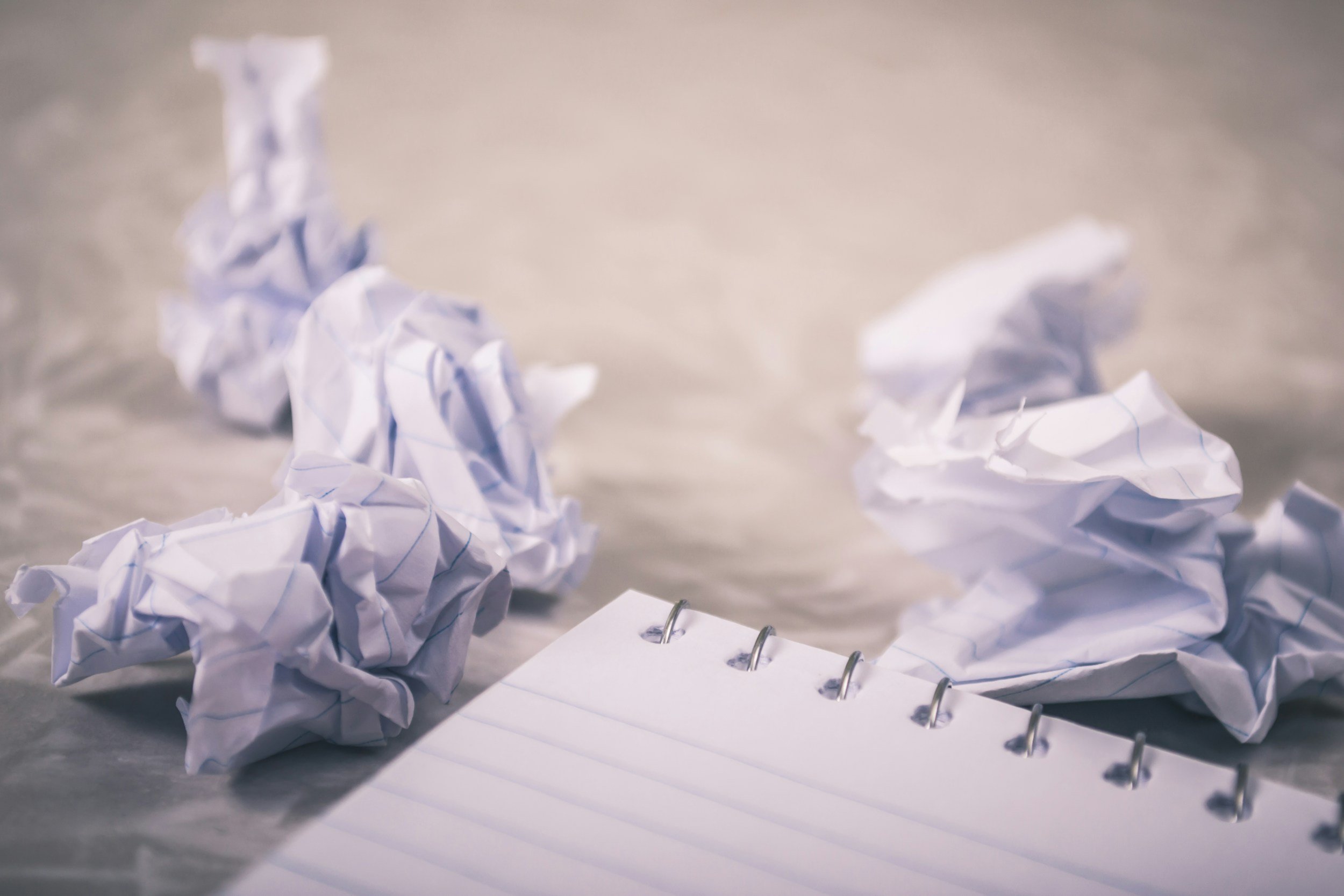Image is of an empty spiral bound notepad. Next to the notepad are numerous balls of paper.