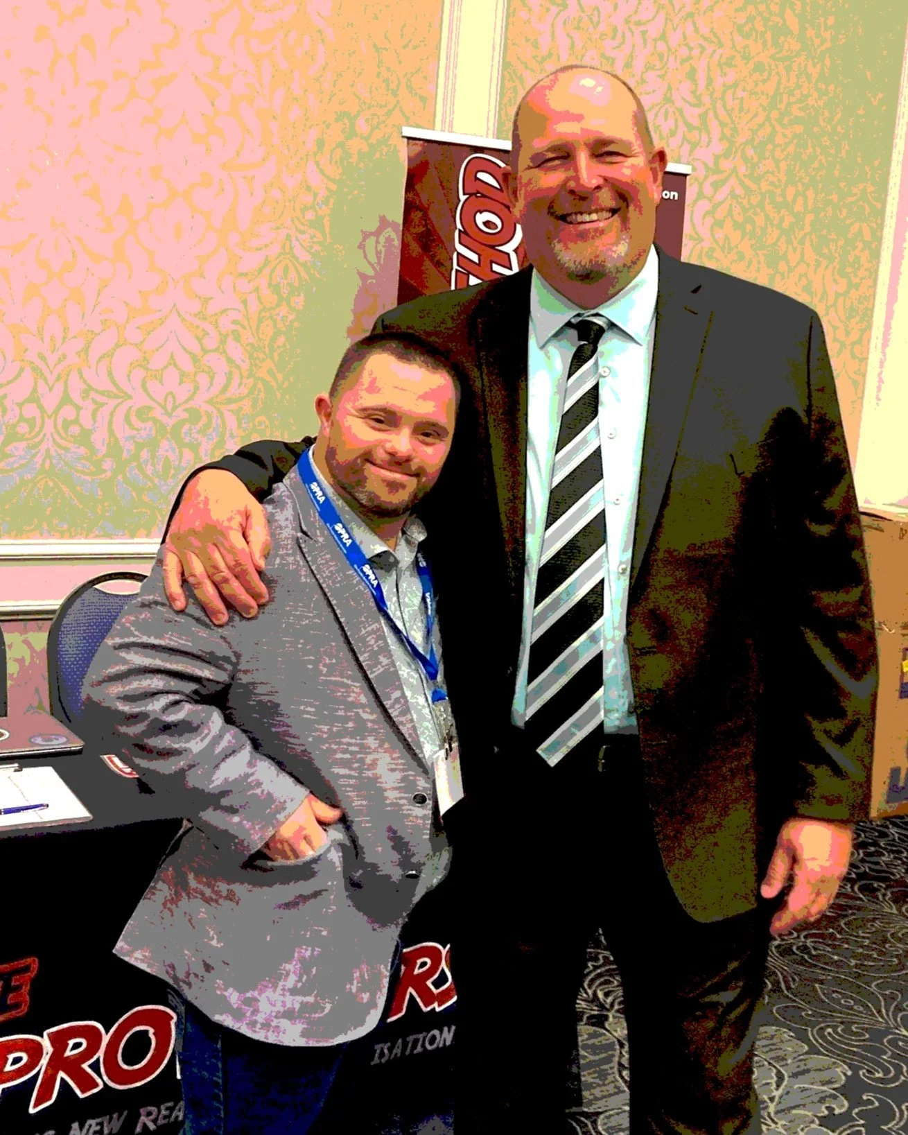 Young man with Down syndrome in a suit stands next to an interviewer smiling.
