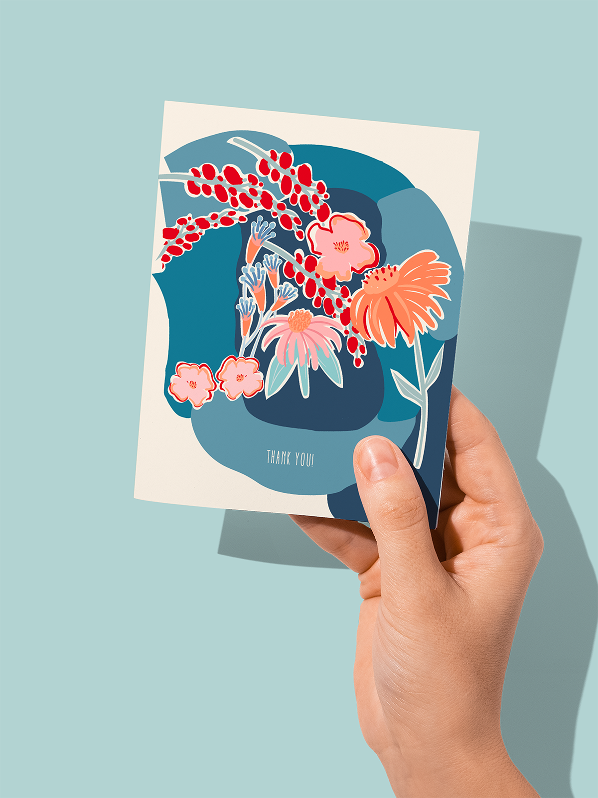 Hand holding a thank you card with an abstract floral design in shades of blue, pink, red, and orange against a light blue background.