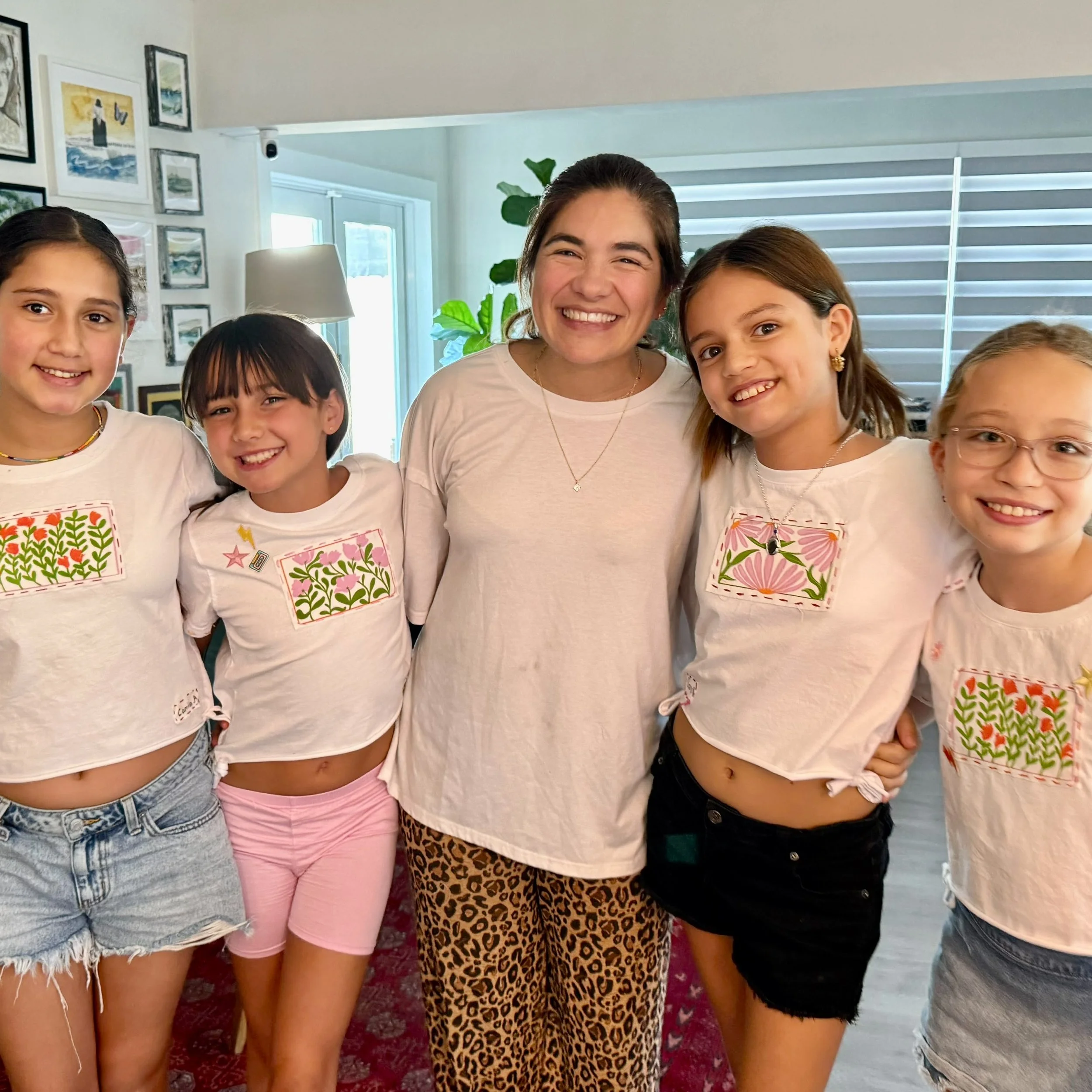 Group of young girls and a woman smiling indoors, wearing casual clothing with colorful patterns and graphics