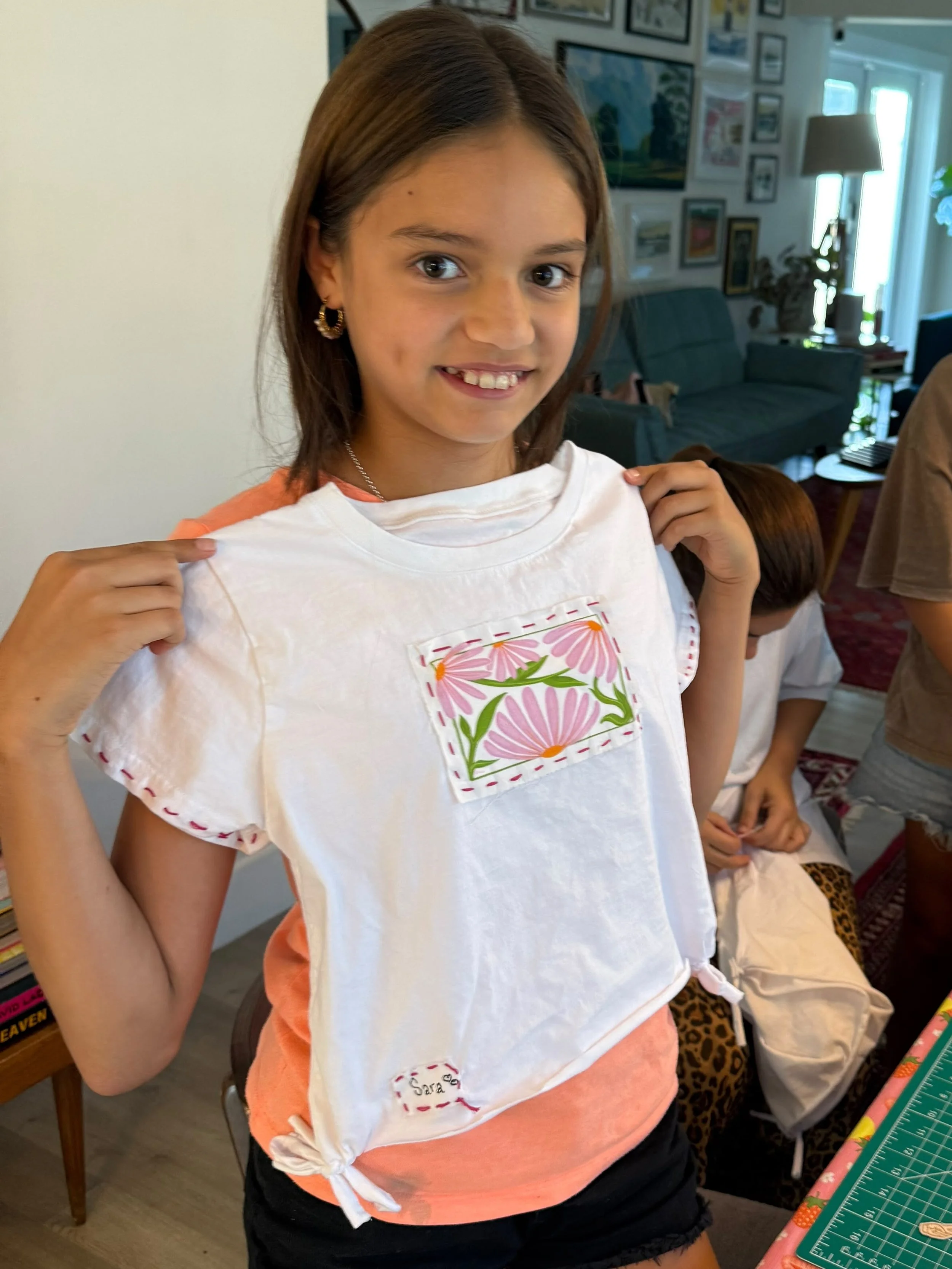 I girl with a t-shirt in her hands that has an illustrated patch and embroidery around it.