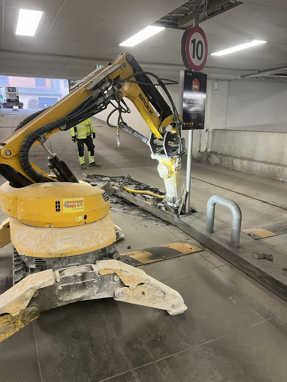 Brokk rivemaskin med betongknuser i parkeringshus