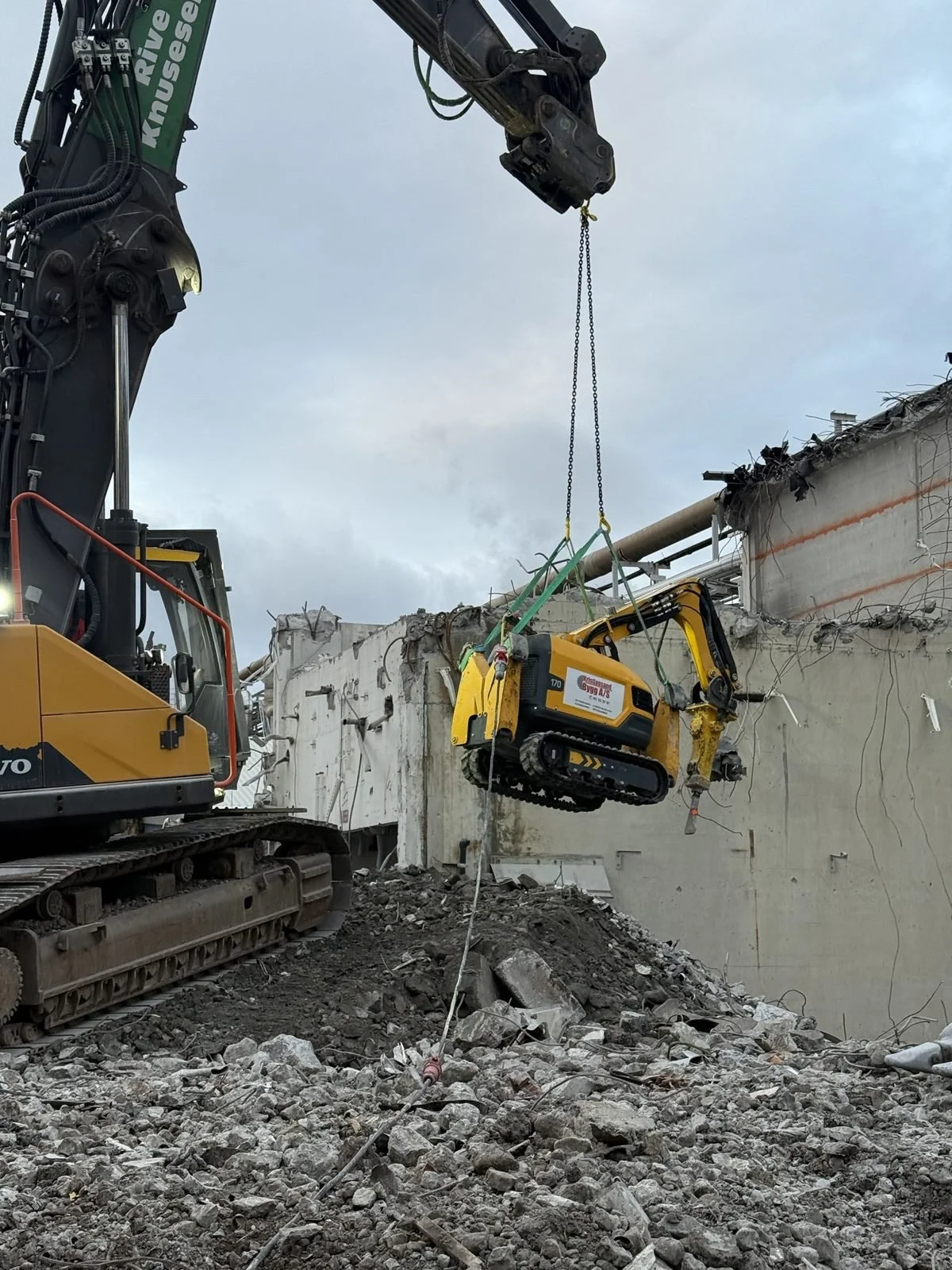 Brokk rivemaskin løftes med kran ned i rivningsområdet
