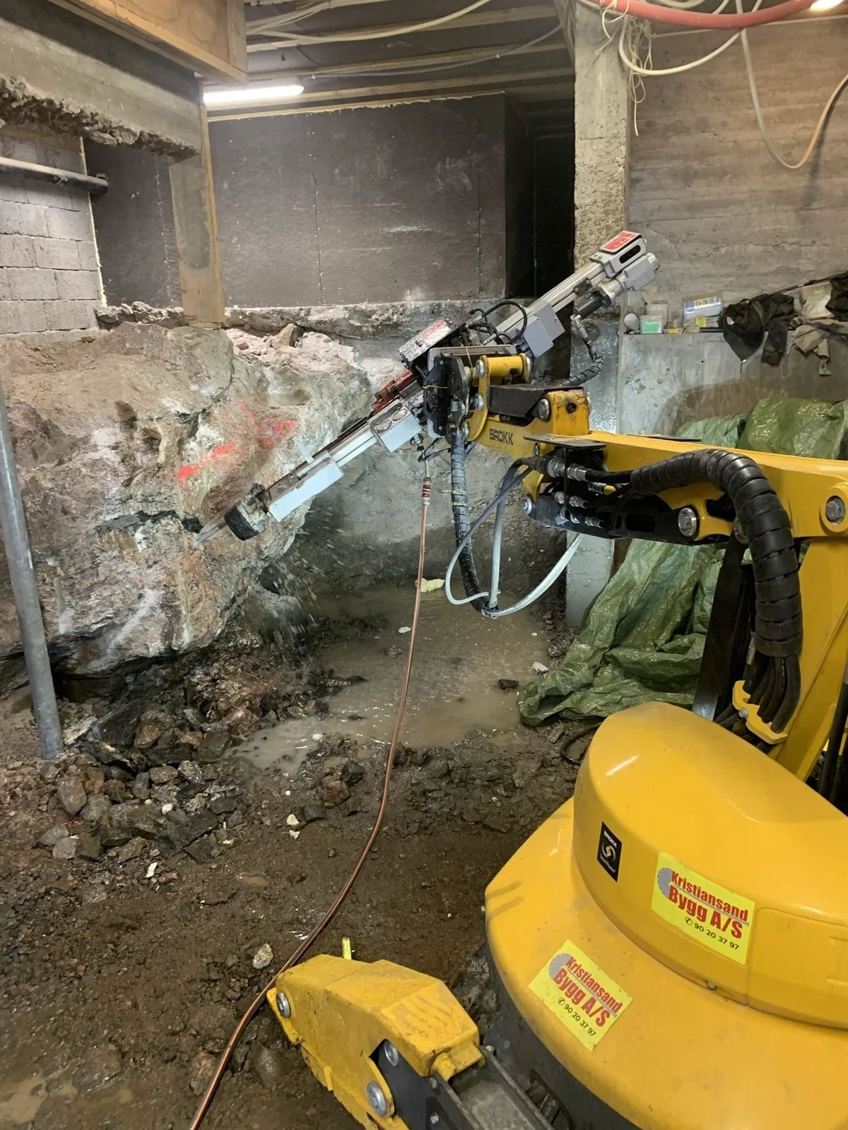 Brokk med borrigg på maskinarmen mot fjell