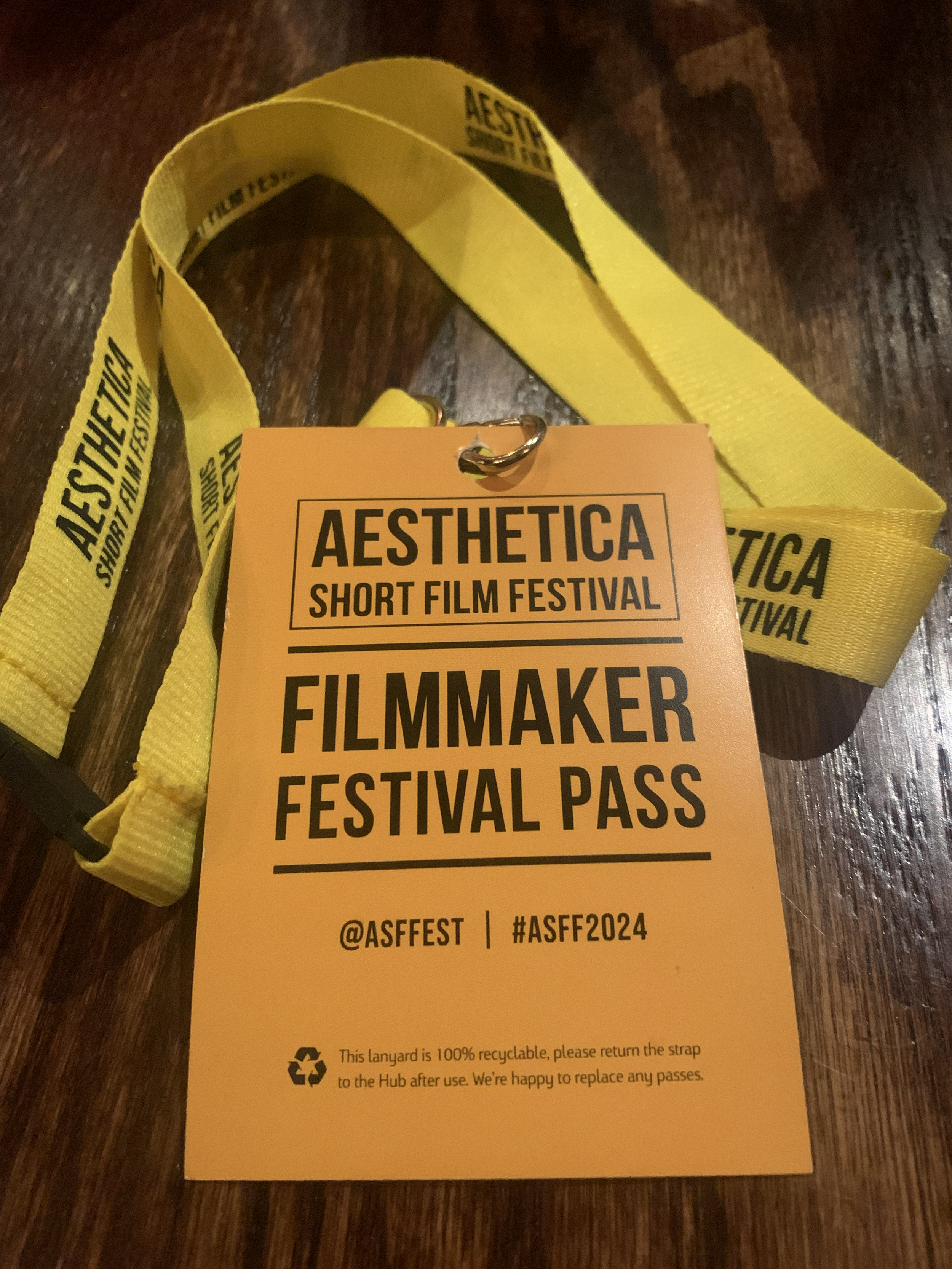 'AESTHETICA SHORT FILM FESTIVAL' layard in yellow with black writing. The pass has the same text, along with social media handles '@ASFFEST' and hashtag '#ASFF2024'. The background is wooden.