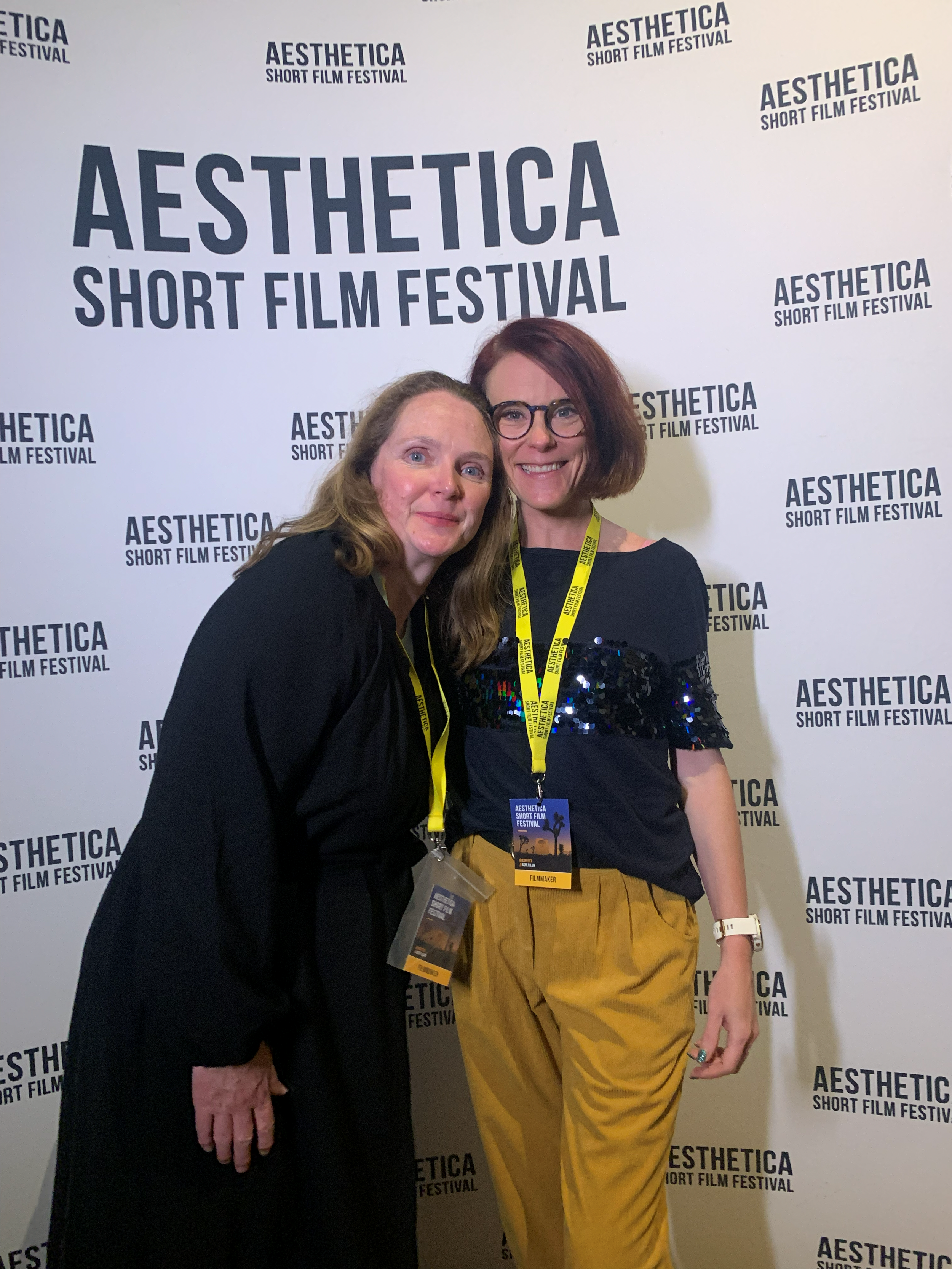 Dee Harvey (Director, Heartbeat) and Johanna Courtney (protagonist, Heartbeat) smiling and posing in front of a backdrop that reads "AESTHETICA SHORT FILM FESTIVAL." Both women are wearing yellow festival badges on lanyards around their necks.