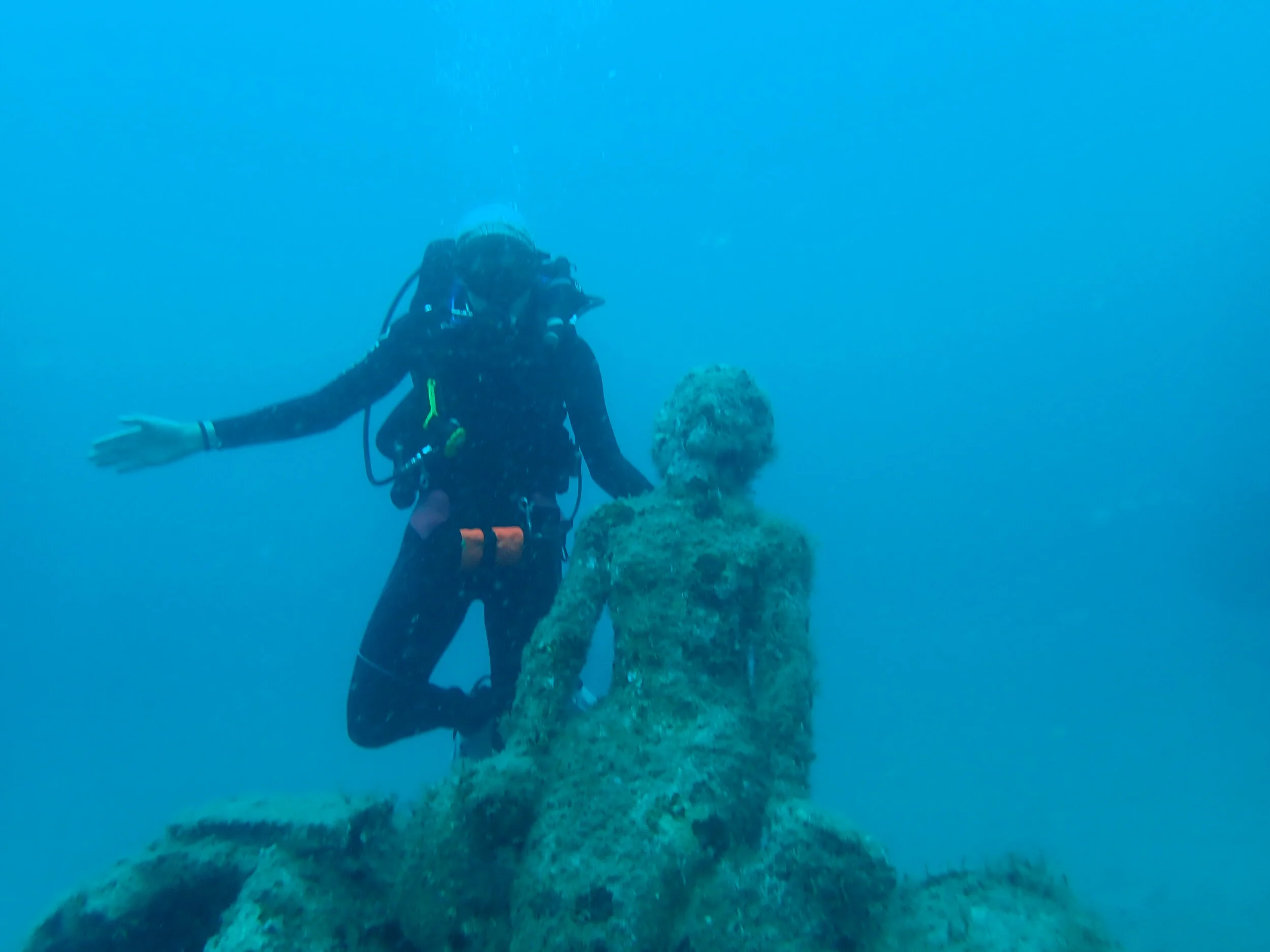 A scuba diver swimming underwater next to a coral-covered statue.