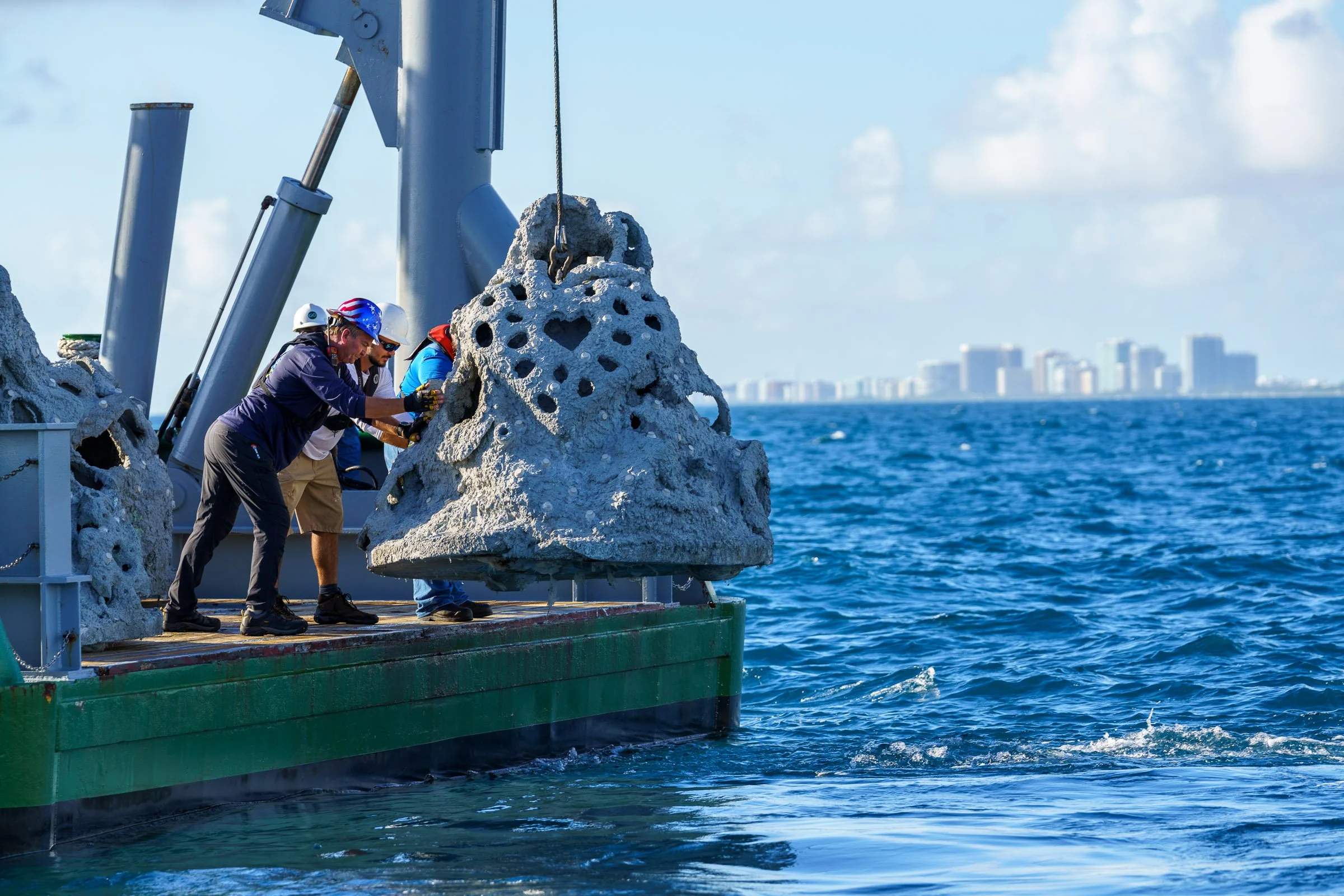 Scientists and engineers in safety gear examine a large coral formation on a research vessel in the ocean.