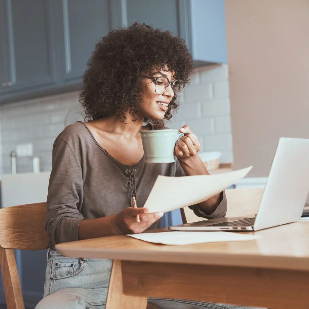 woman with coffee, laptop, and papers, representing creating a debt payoff strategy that works - Mindfully Money Financial Coaching