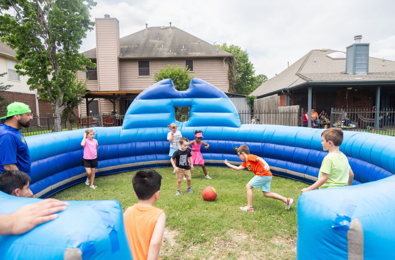 Children playing soccer inside a blue inflatable bounce house in a backyard.