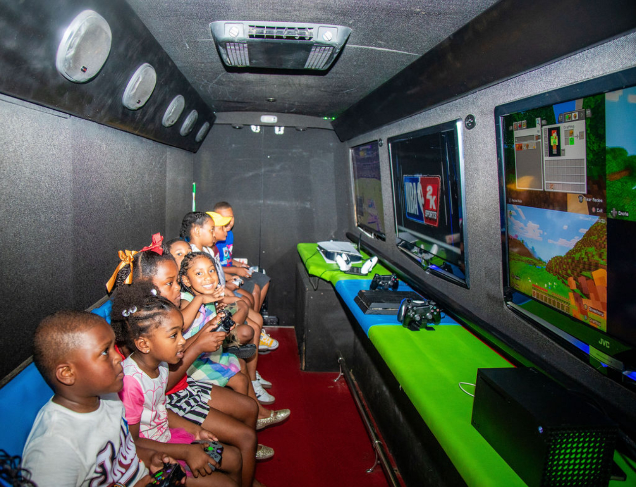 Group of children sitting in a gaming room playing video games on large screens.