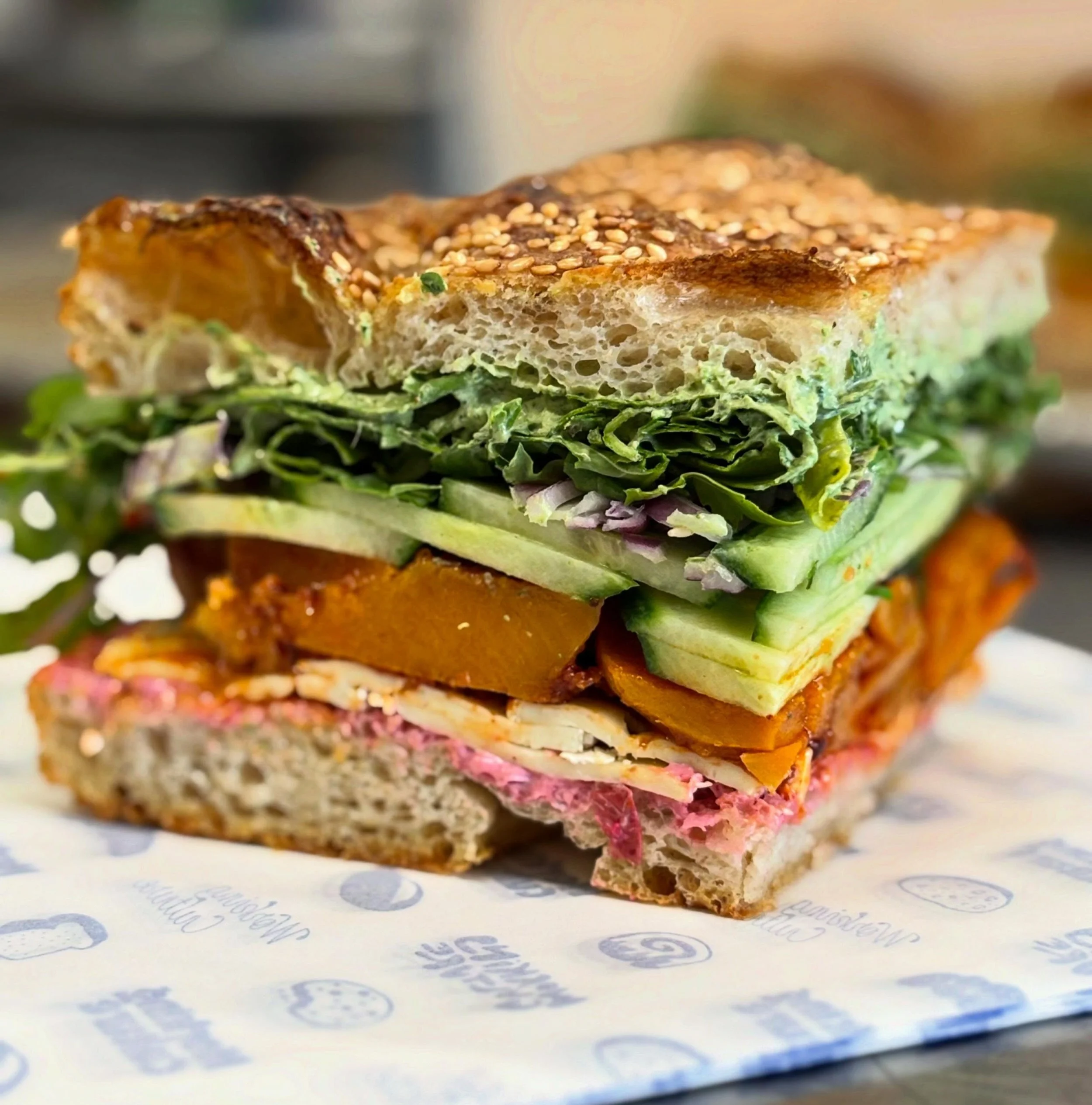 veg focaccia on rotation - roasted butternut squash tossed in chili crunch and cumin, brie, mint chutney sour cream, arugula, cranberry mayo, cucumber, red onion, sourdough sesame focaccia