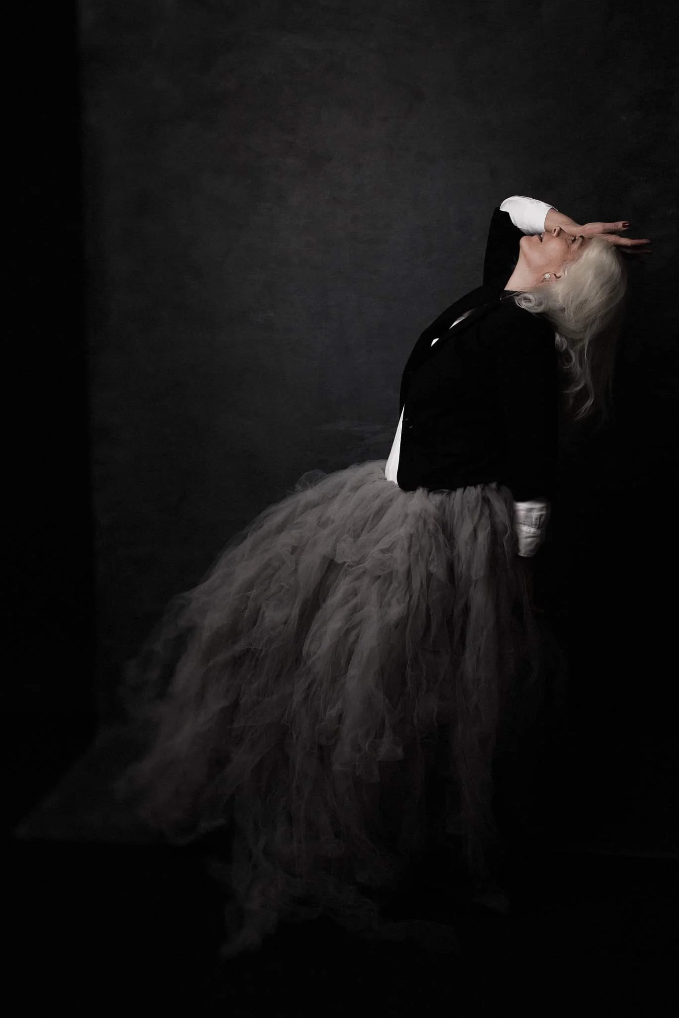 Woman with white hair posing against a black background, wearing a black top and a light, voluminous tulle skirt.