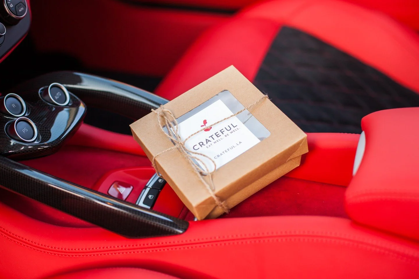 Crateful parting gift box tied with twine resting on the red leather seat of a Ferrari