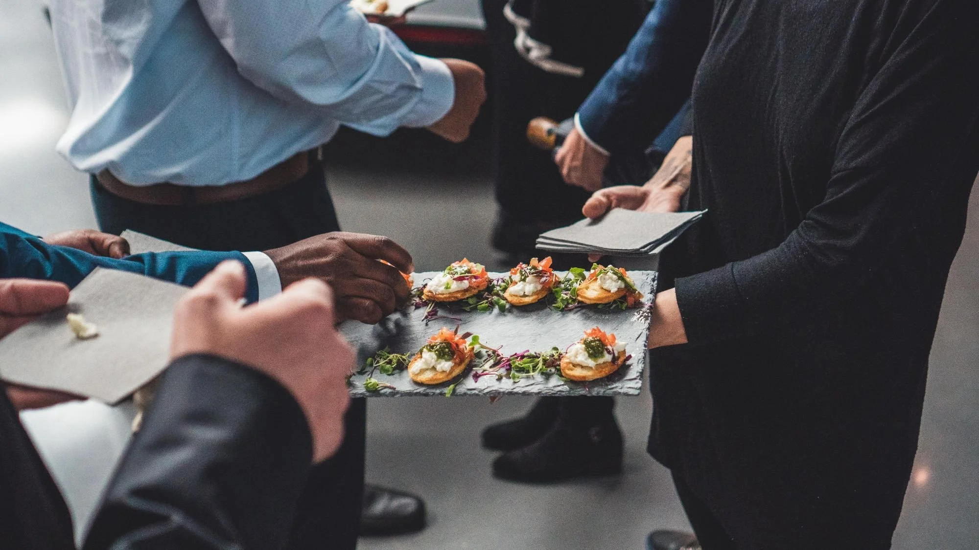 Guests taking passed canapes from a slate tray during a formal reception