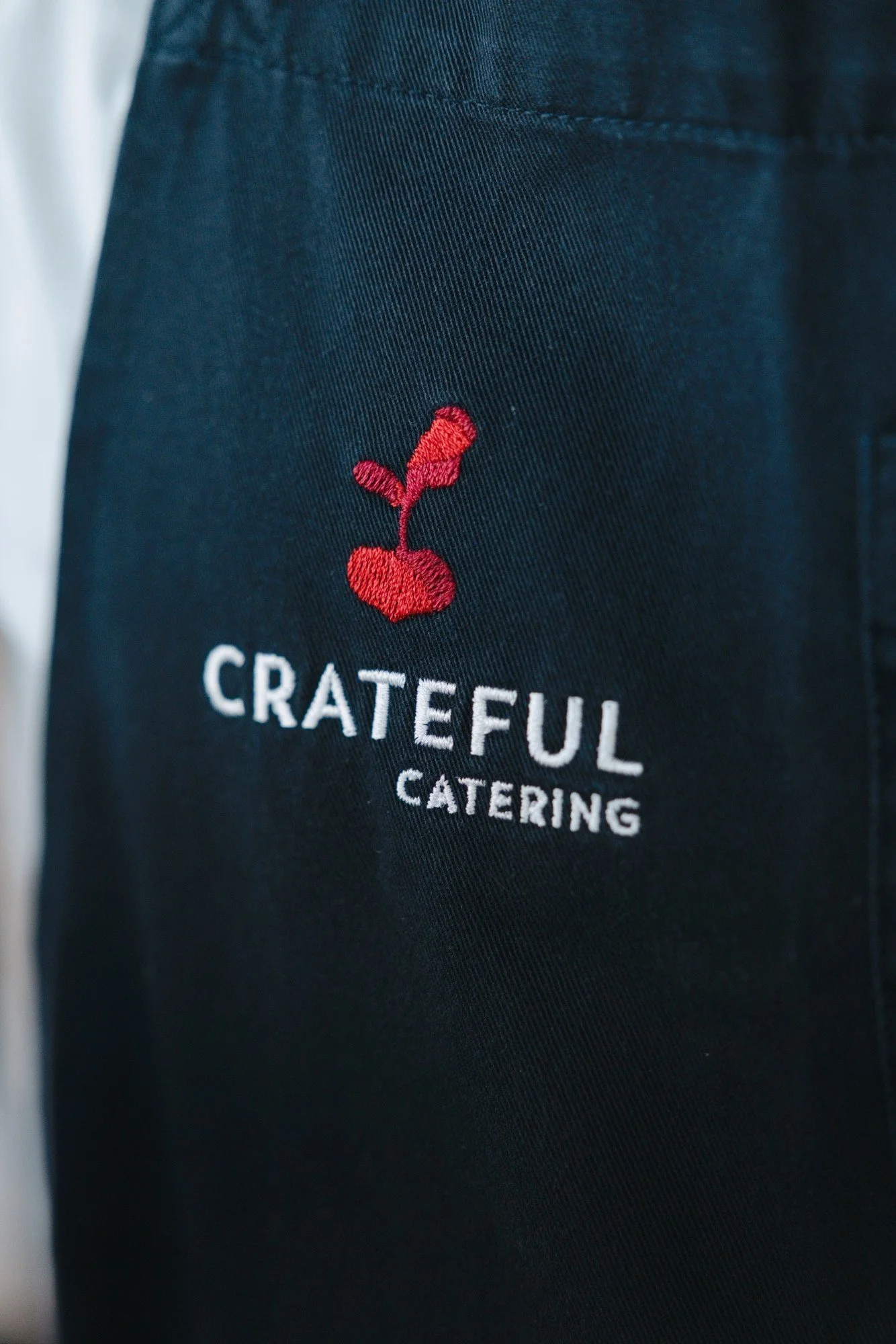 Close-up of the Crateful Catering logo embroidered on a navy staff apron
