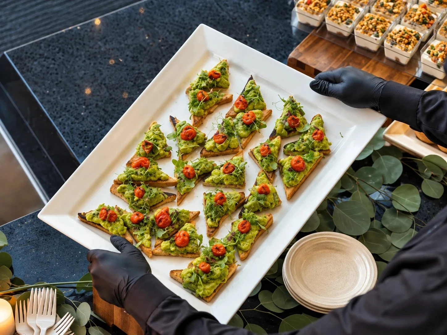 Server presenting a tray of avocado toast points with cherry tomato confit and microgreens