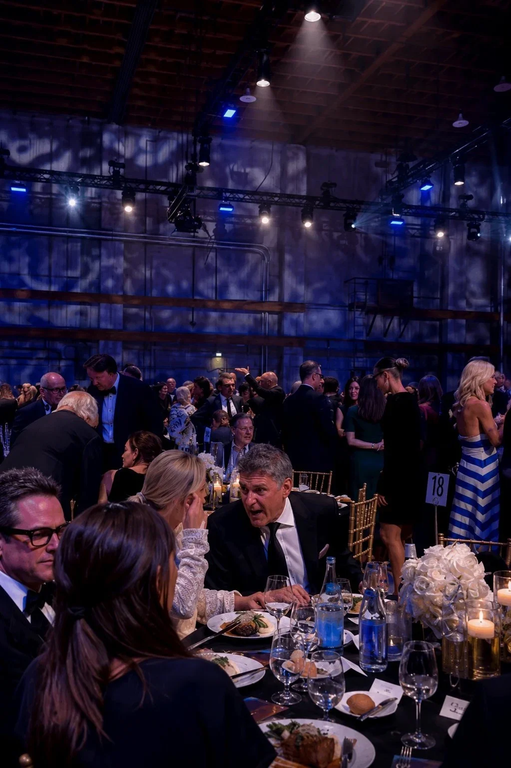 Black-tie guests seated at a formal gala dinner in a large event hall