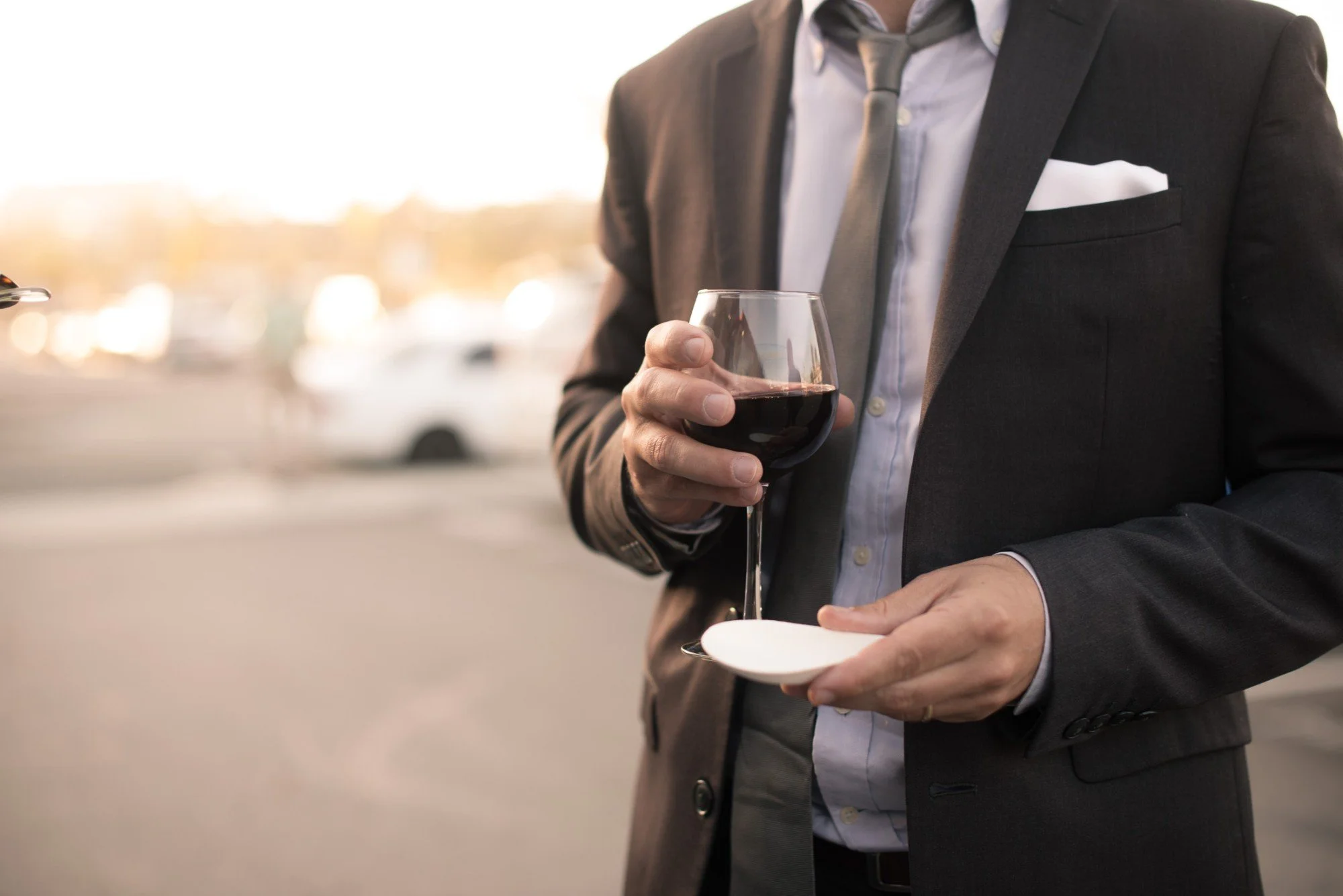 Guest in a suit holding a glass of red wine and a small plate at an outdoor reception