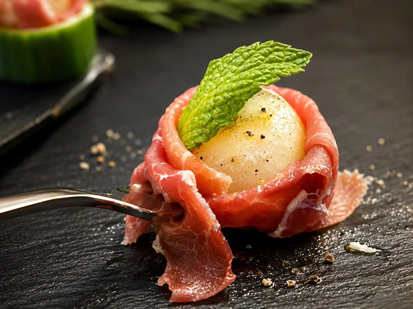Close-up of a prosciutto-wrapped melon appetizer garnished with fresh mint