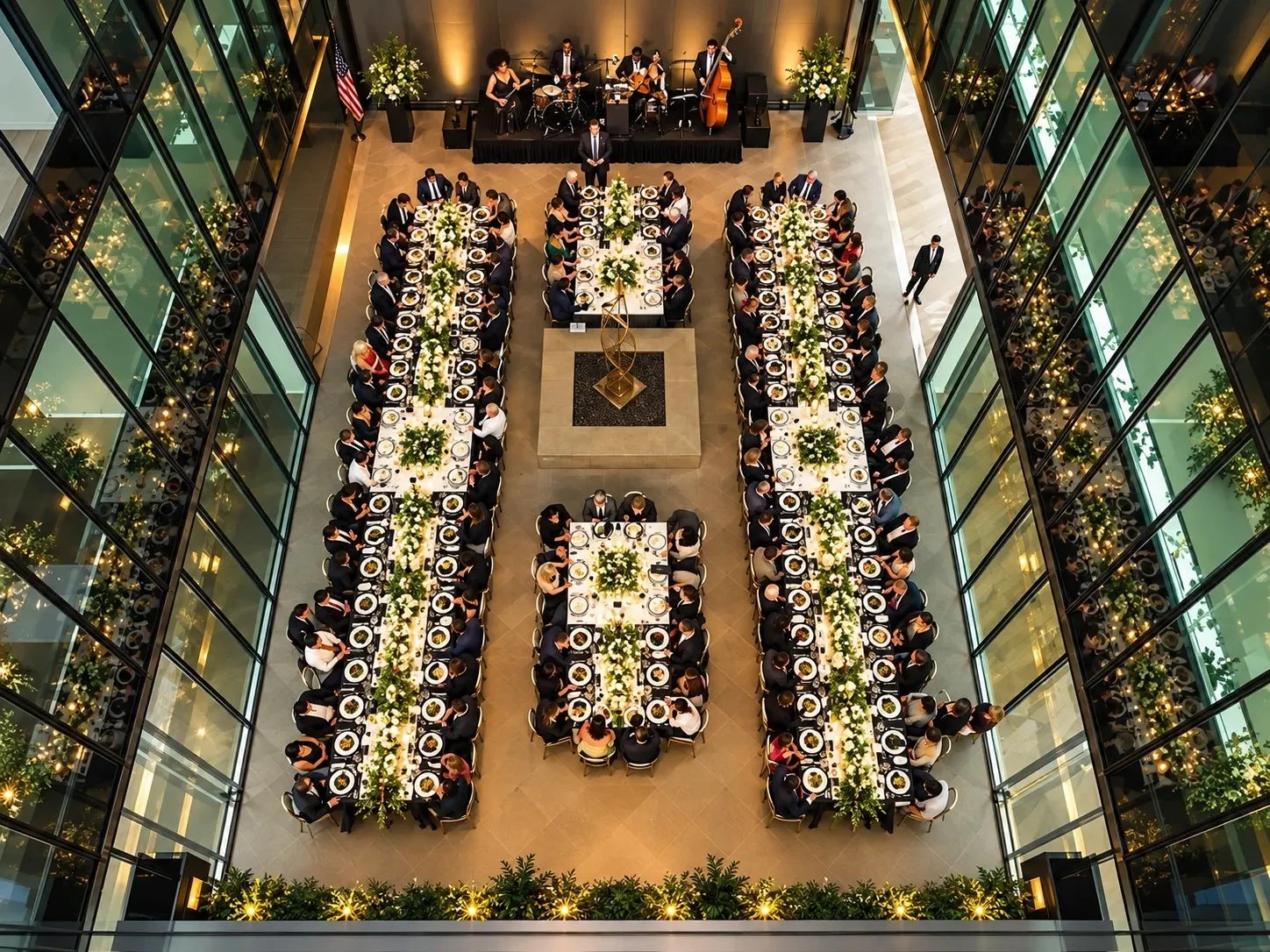 Aerial view of long banquet tables and a live band at a formal dinner in a glass atrium