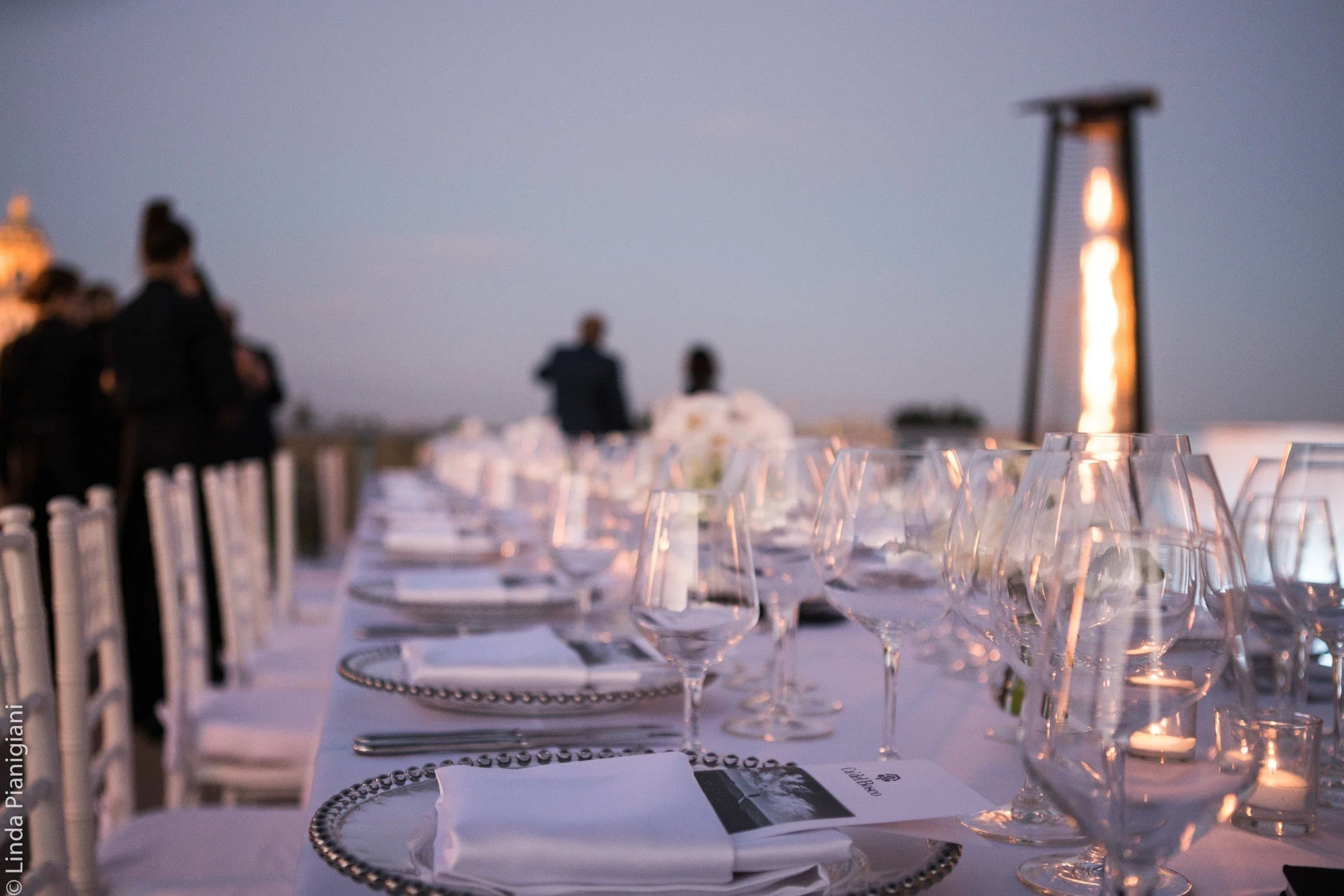 Long formal dining table set with crystal glassware and printed menus at dusk