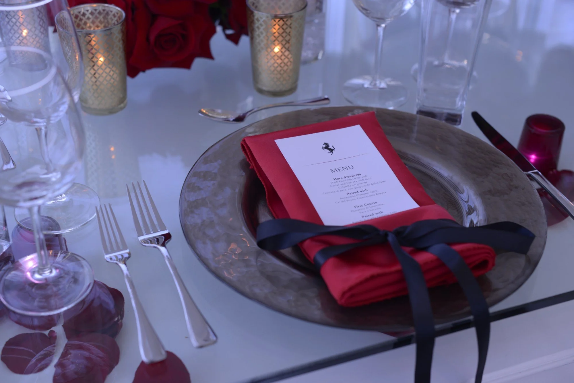 Ferrari-branded menu card on a red napkin at a candlelit place setting with roses and crystal