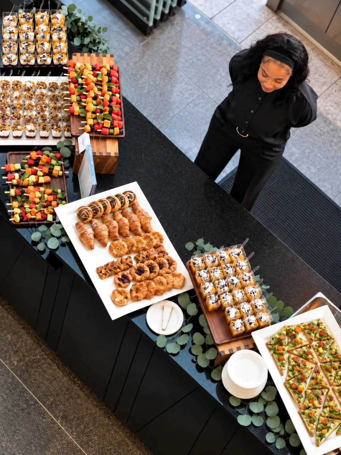 Overhead view of an office lobby breakfast buffet with parfait cups, fruit skewers, pastries and avocado toast