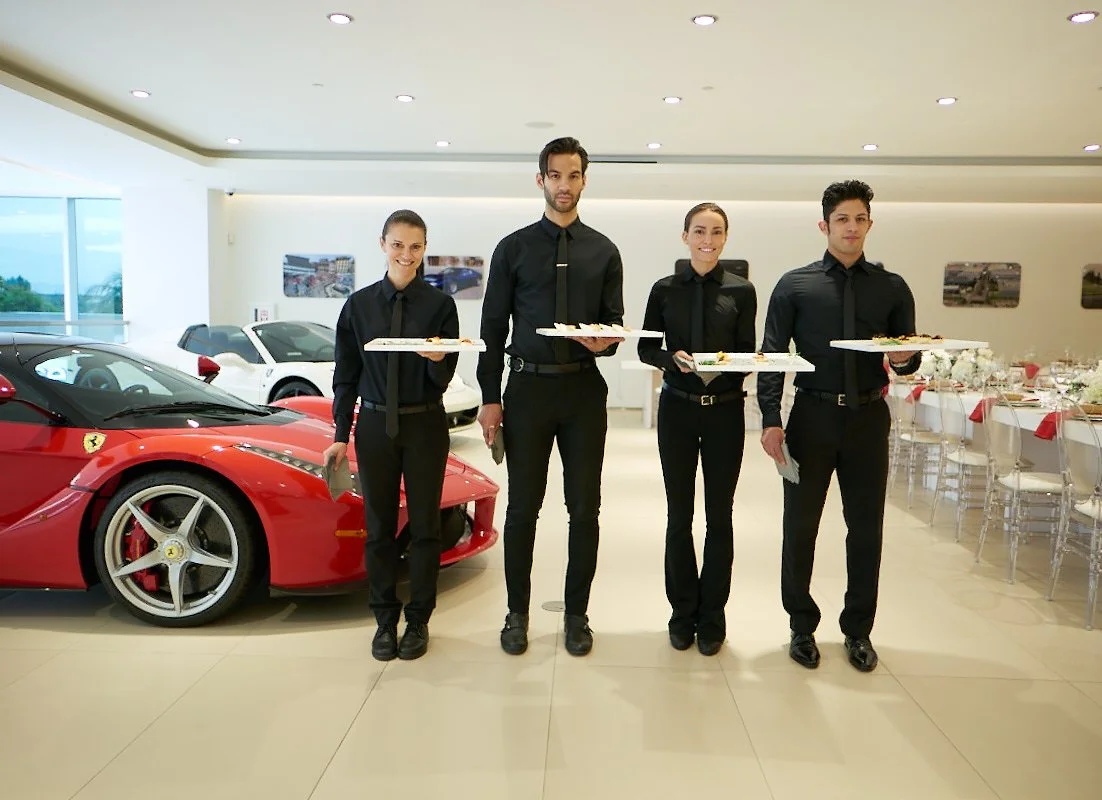 Four Crateful servers in black uniforms holding canape trays in the Ferrari showroom before service
