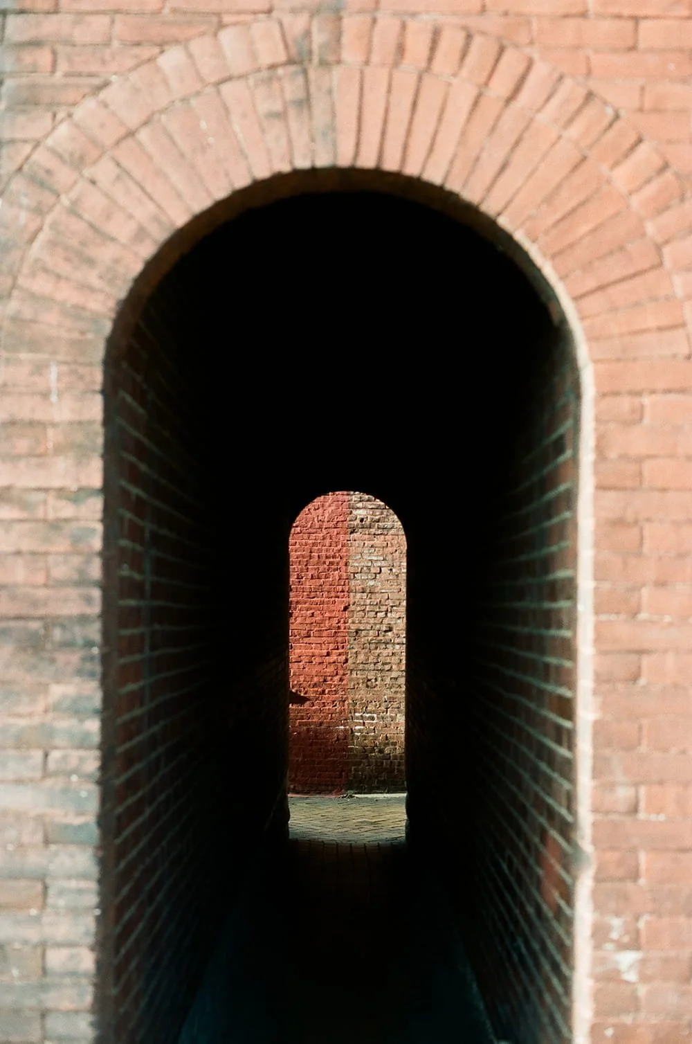 A series of brick archways creating a tunnel effect, with the innermost arch illuminated by sunlight.