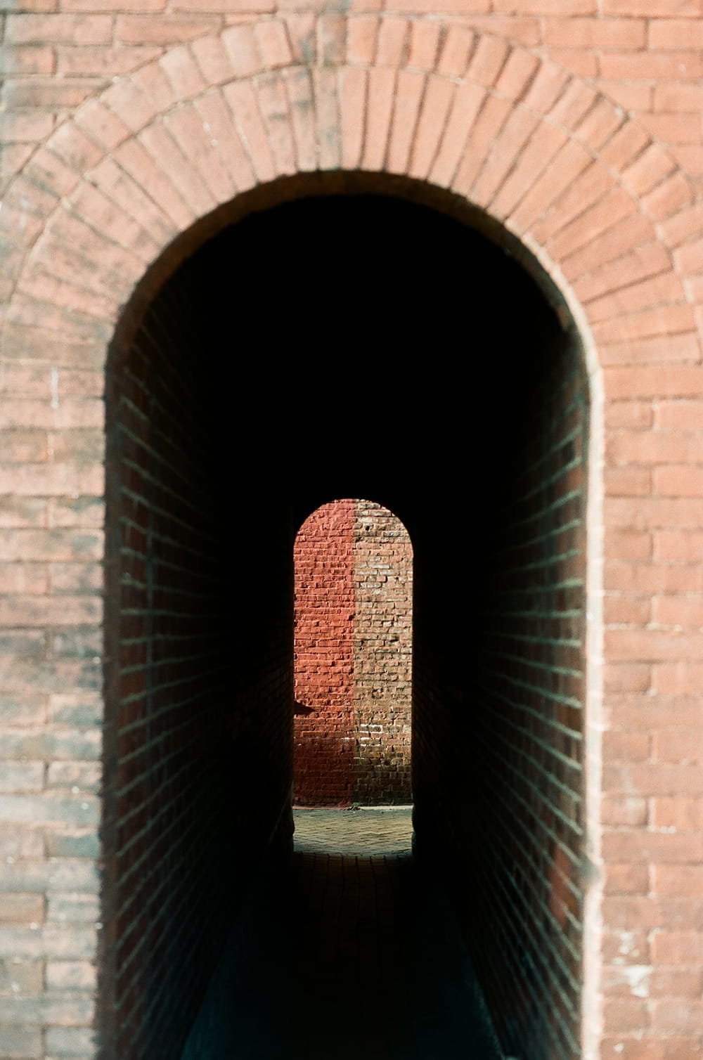 A series of brick archways creating a tunnel effect, with the innermost arch illuminated by sunlight.