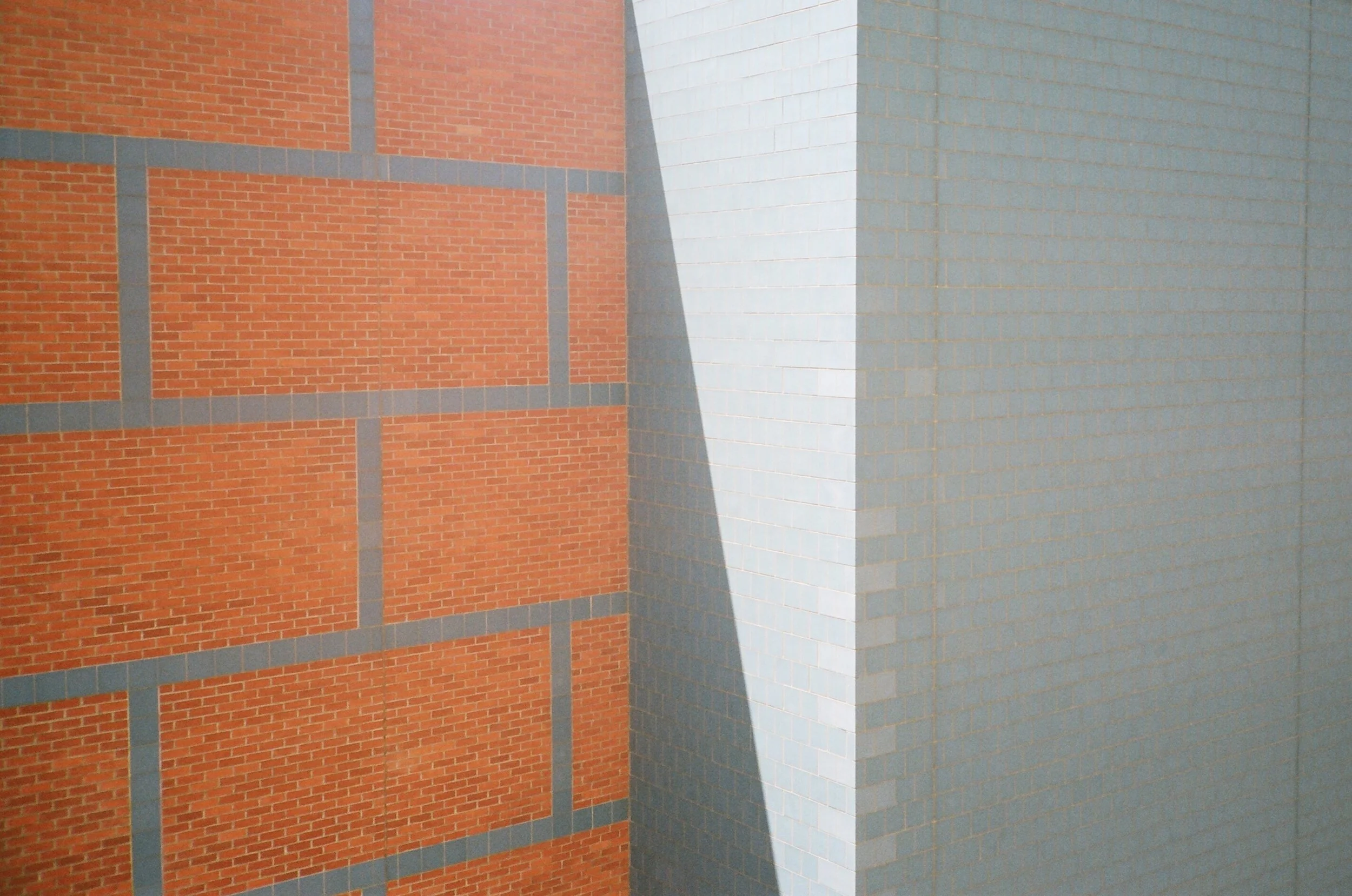 Close-up of a building corner with red brick, gray concrete lines, and white and light blue tiled surfaces.
