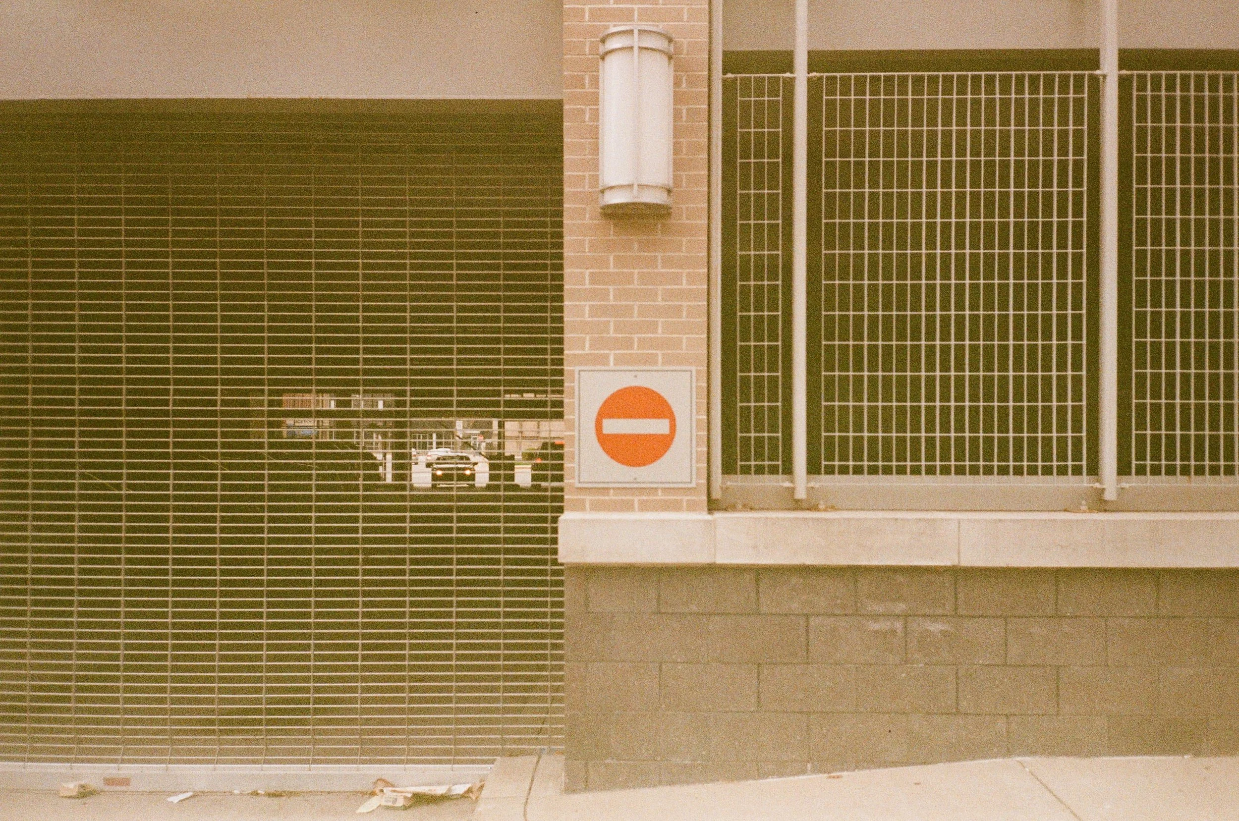 A building’s exterior wall with a brick section and a metal gate, featuring a white utility box and a 
