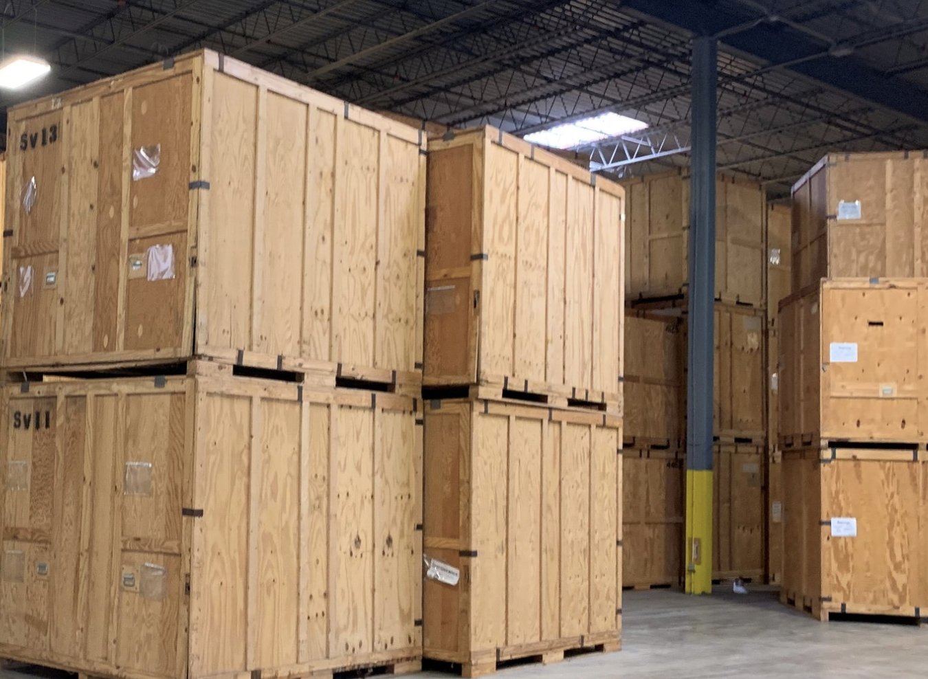 Stacked wooden crates inside a warehouse with metal ceiling and support beams.