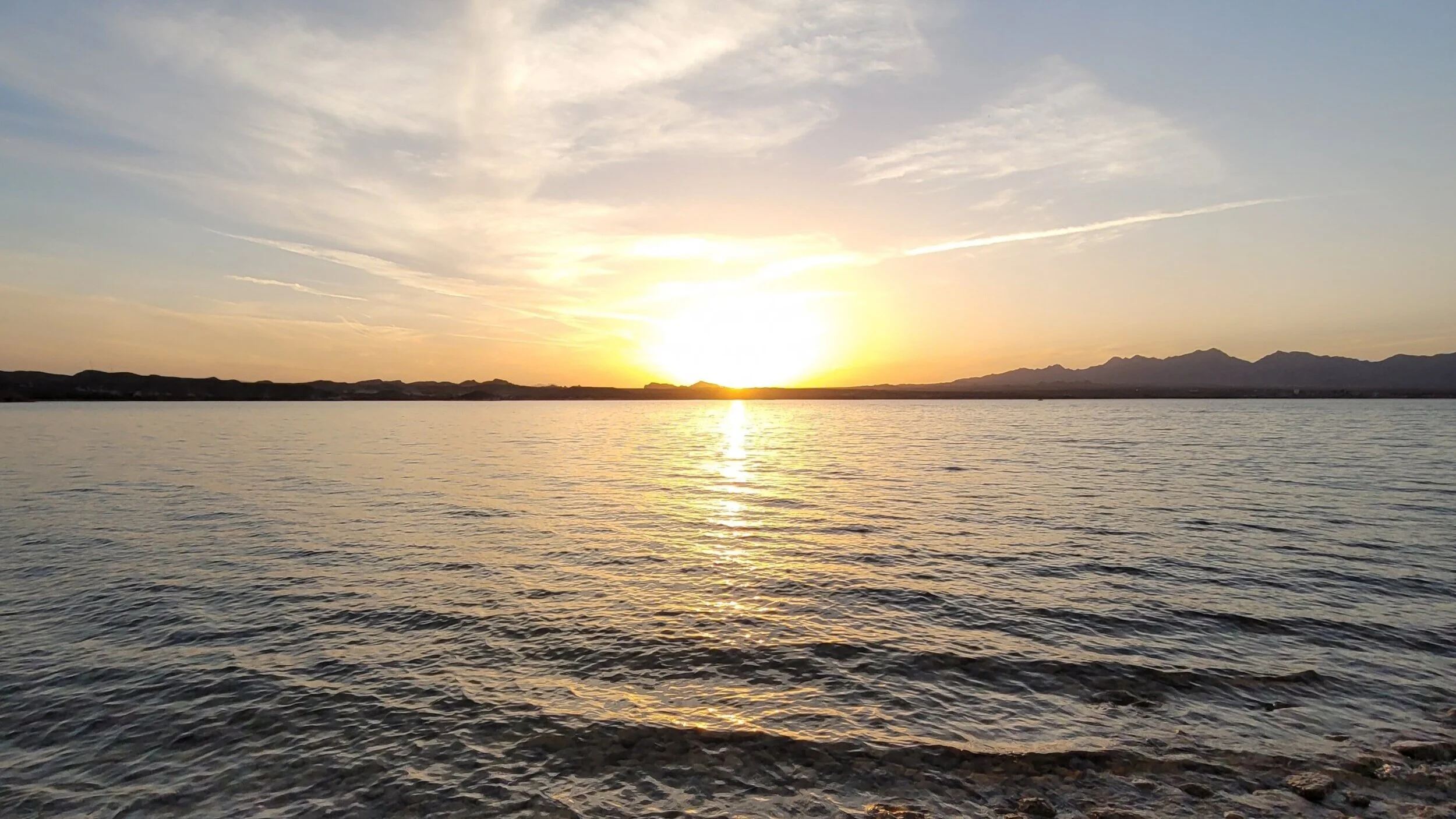 Sunset over a calm lake with mountains in the background and a clear sky.