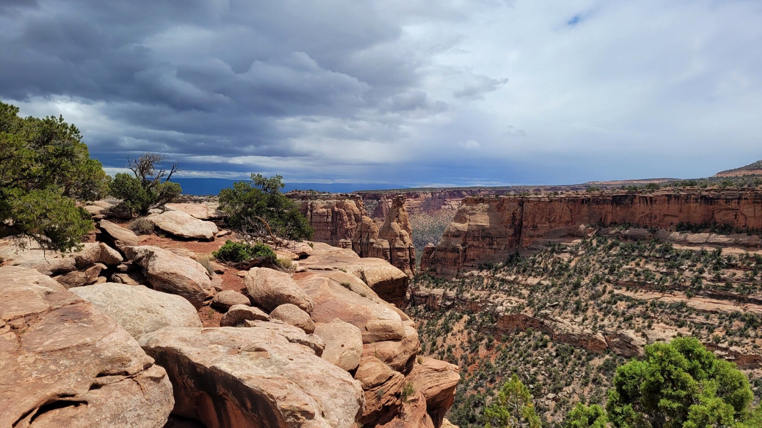 Scenic view of a rocky desert canyon with cliffs and scattered vegetation under a cloudy sky.