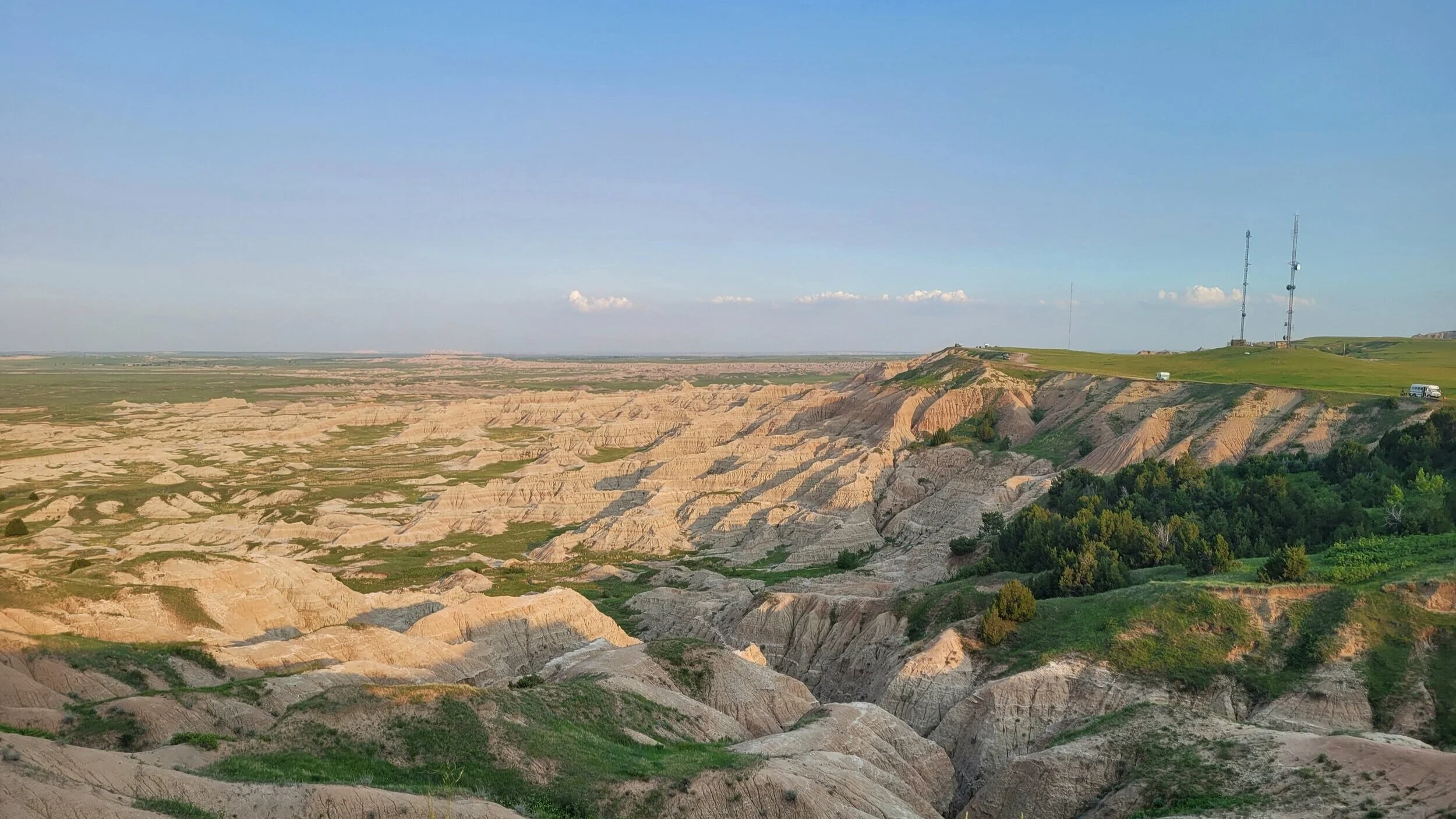 Landscape of Badlands with rugged rock formations, green vegetation, and clear blue sky.