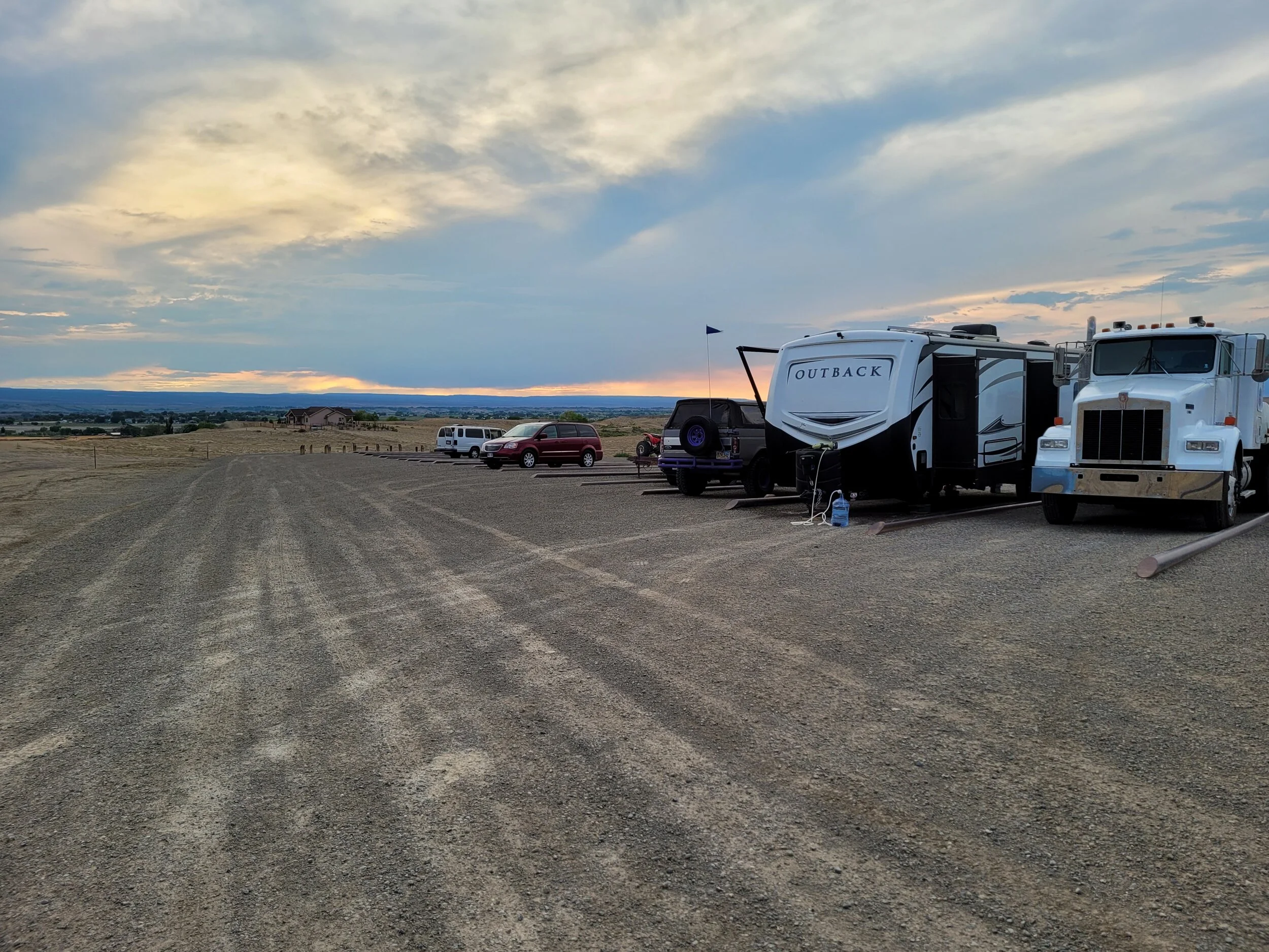 Gravel lot with parked RVs, truck, and cars at sunset