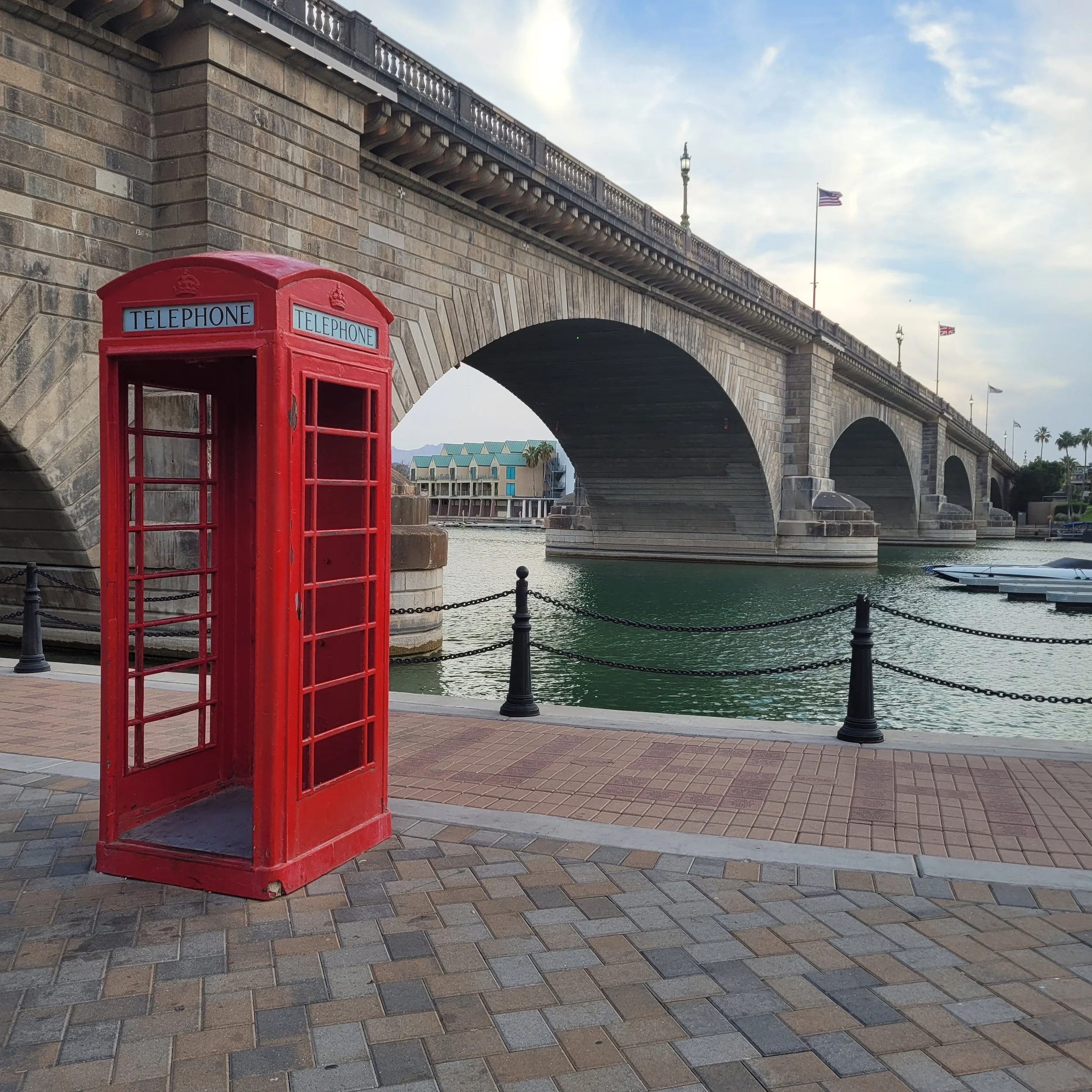 Red telephone booth near a stone bridge over water under a blue sky.