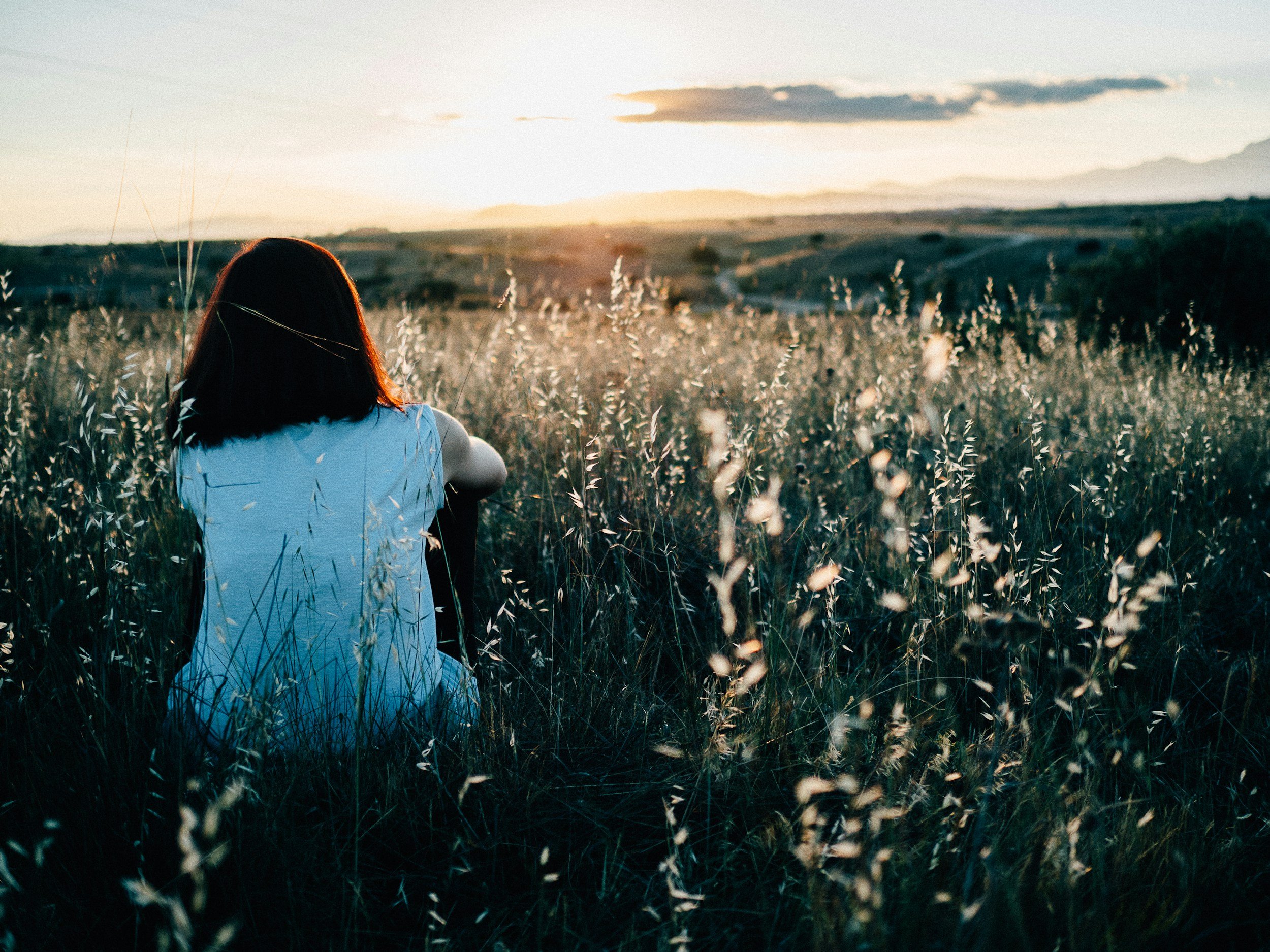Lonely woman sitting in a field of grass watching the sun set